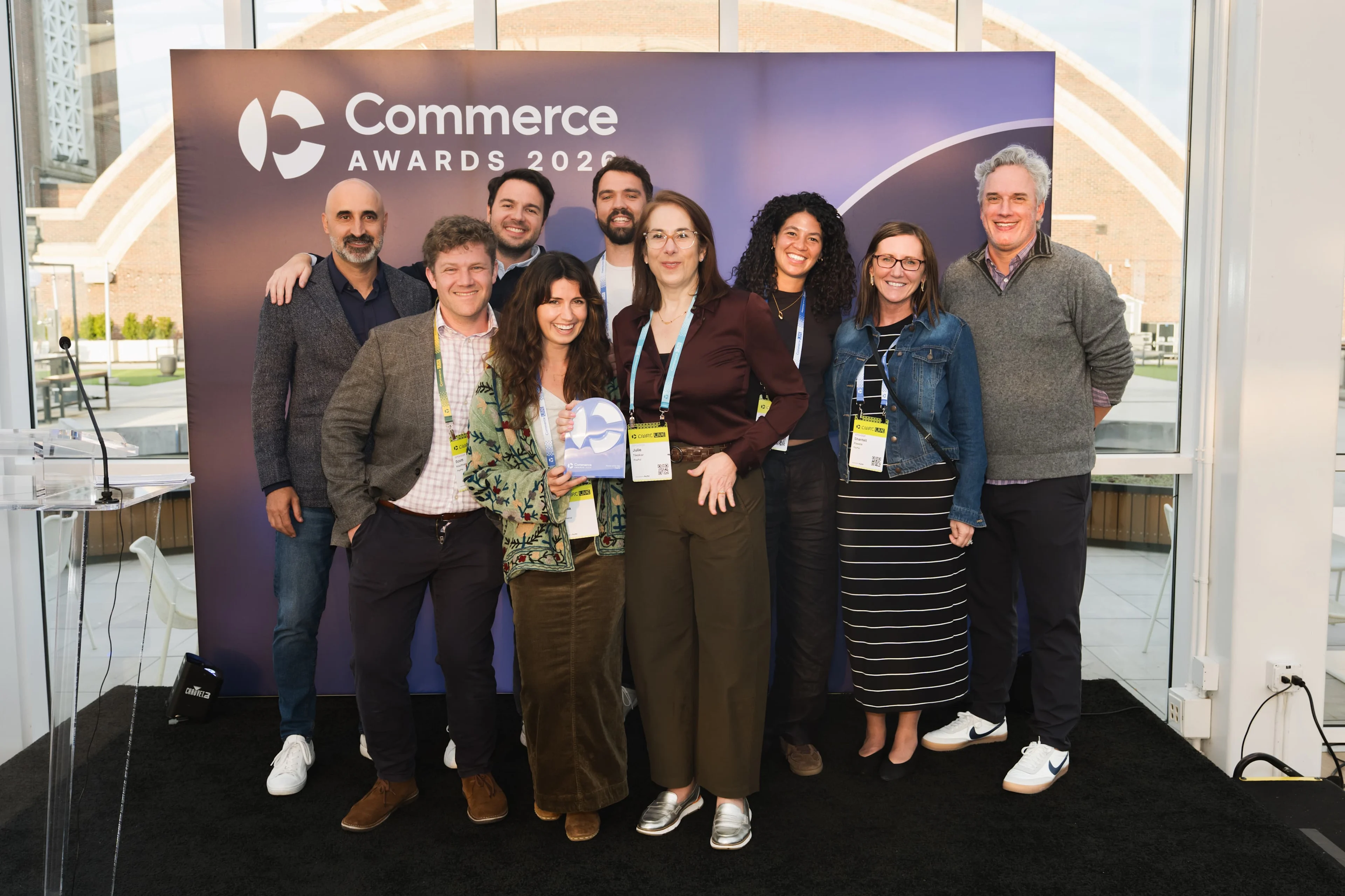 PayPal wins Tech Partner of the Year at the Commerce Awards 2026. Group of eight smiling award attendees posing with a trophy in front of a “Commerce Awards 2026” backdrop.