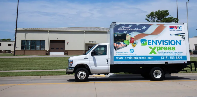 White Envision Xpress delivery truck parked on street in front of warehouse under blue sky.