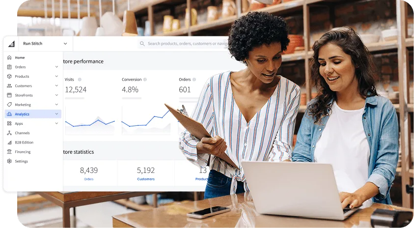 Two women review analytics on a laptop in a store, with charts and performance data displayed on the screen.