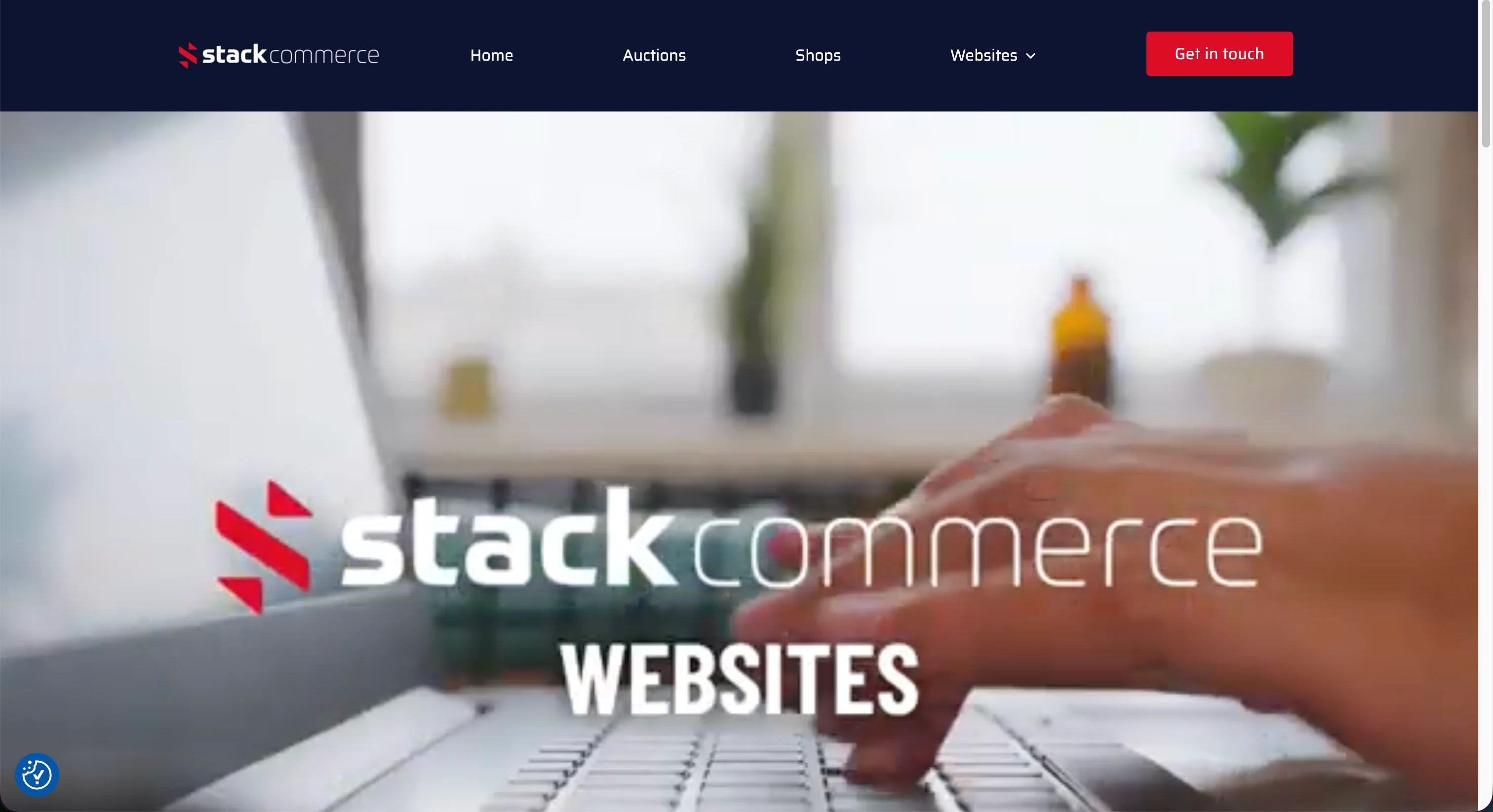 Stackcommerce website page showing navigation bar and “Get in touch” button over a blurred hand typing on a laptop.