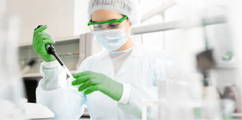 Laboratory technician wearing protective gloves and mask using a pipette to handle samples in a clinical research setting.