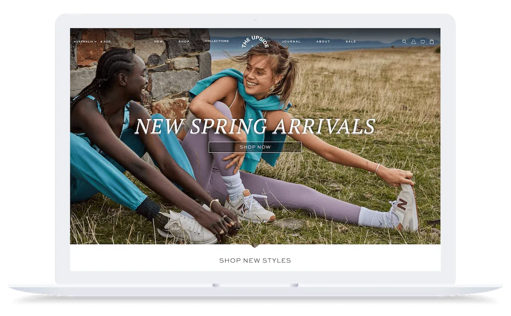 Two women in colorful activewear sit and smile outdoors on grass, with text reading "New Spring Arrivals" on the screen.