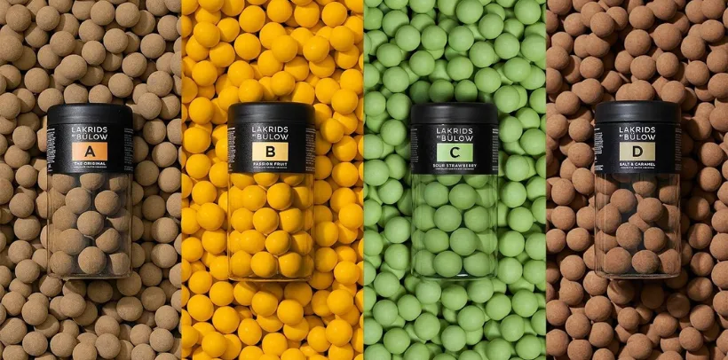 Four jars of Lakrids by Bülow licorice, each on matching colored candies: brown, yellow, green, and brown.