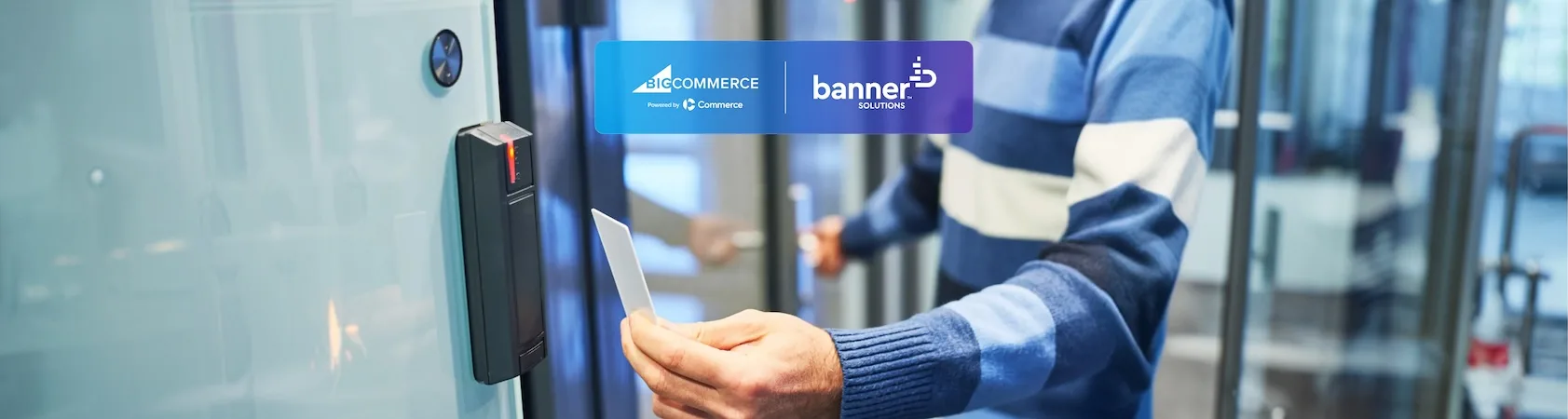 Person in blue sweater holding white card near black card reader at glass door with BigCommerce and Banner Solutions logos