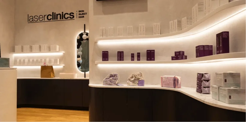 Modern laser clinic reception area with curved white shelving displaying skincare products, illuminated by LED strip lighting.