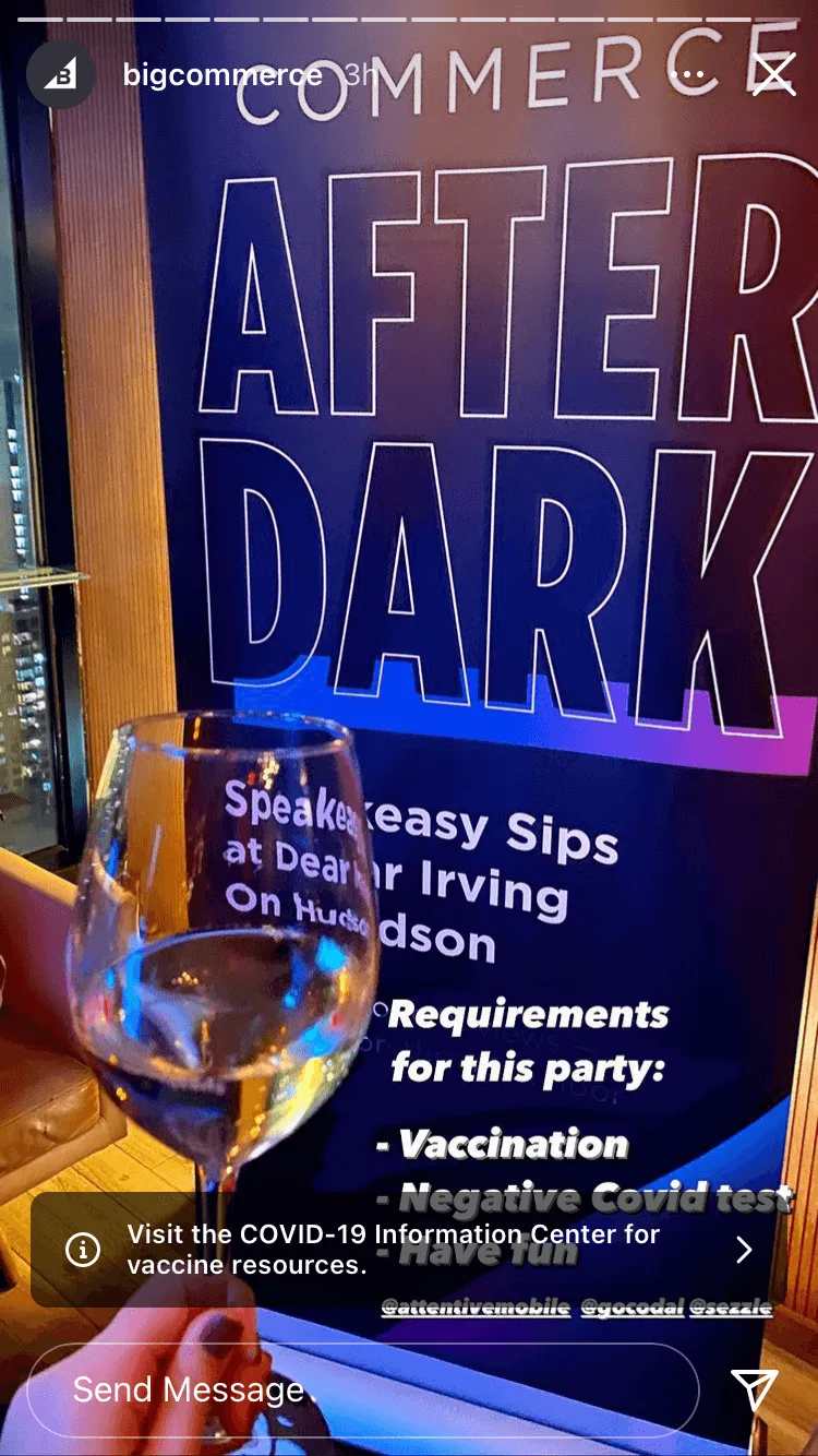 A wine glass held in front of a blue "After Dark" event sign with COVID-19 safety requirements listed.