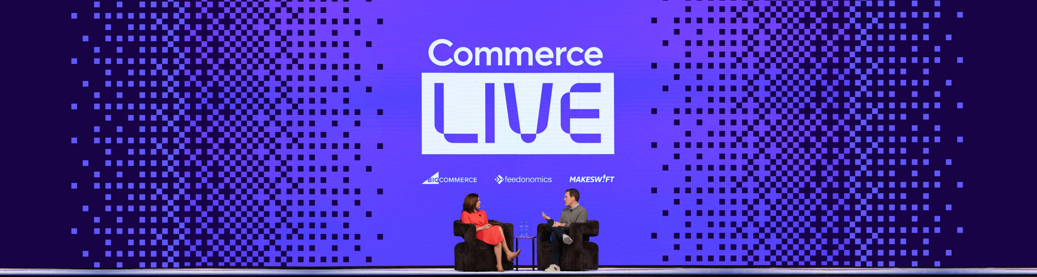 Two speakers seated on stage beneath “Commerce LIVE” on a purple pixelated backdrop, with sponsor logos above.
