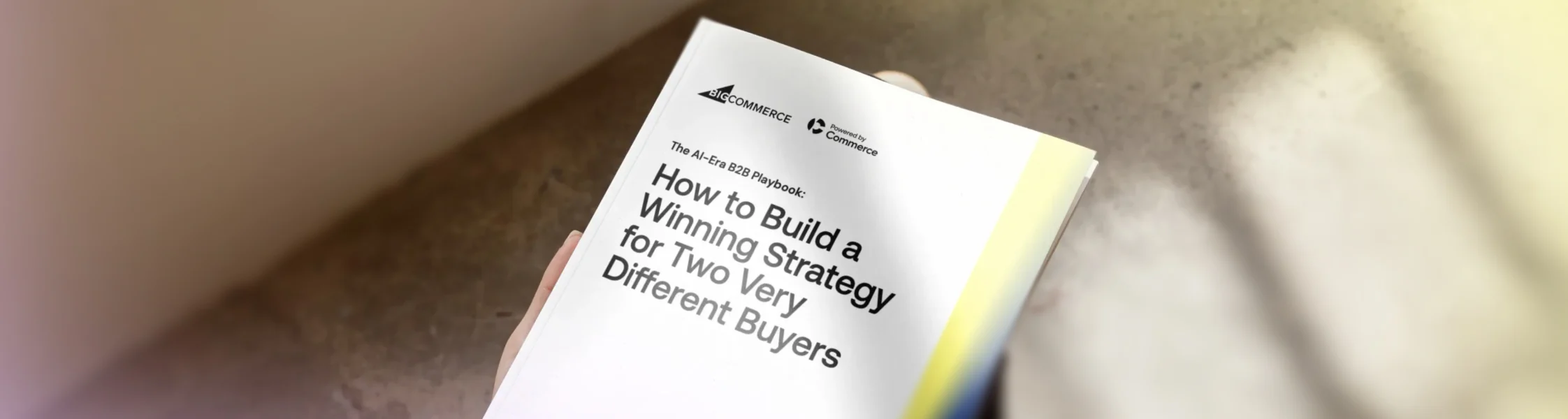 Hand holding white B2B playbook titled "How to Build a Winning Strategy for Two Very Different Buyers" on concrete surface.