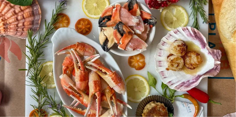Assorted seafood including crab claws, scallops, and lemon garnishes arranged on white serving dishes.