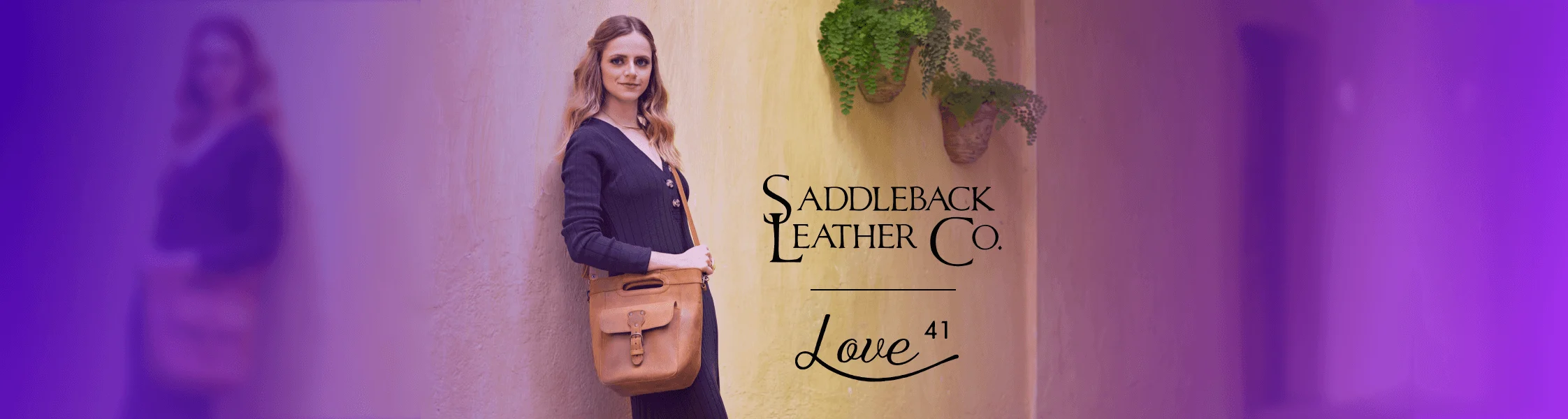 Saddleback Leather Company - Woman in black dress standing against wall with light brown leather bag
