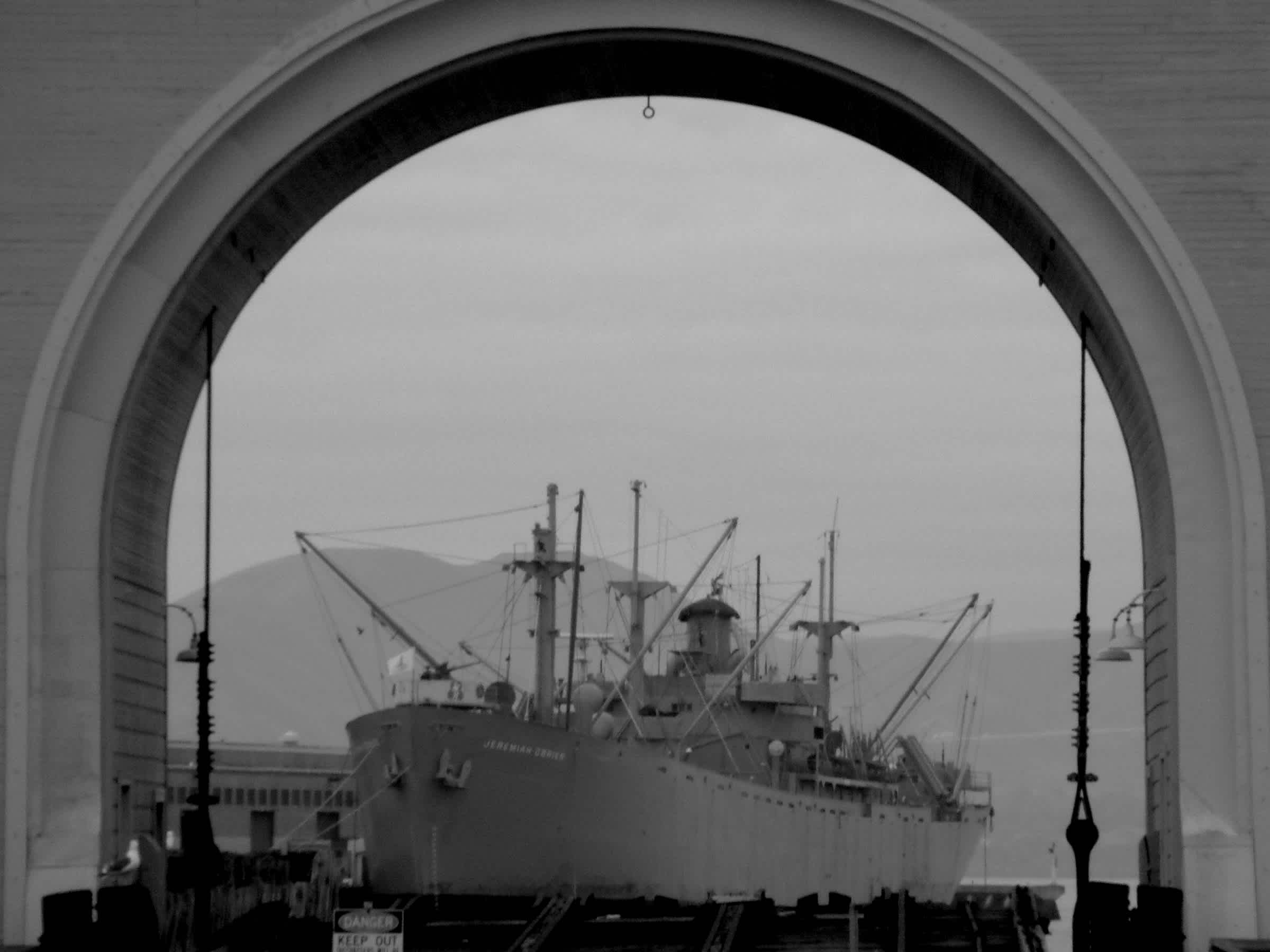 Boat resting in the water underneath building archway in black and white in Embarcadero, San Francisco, California.  