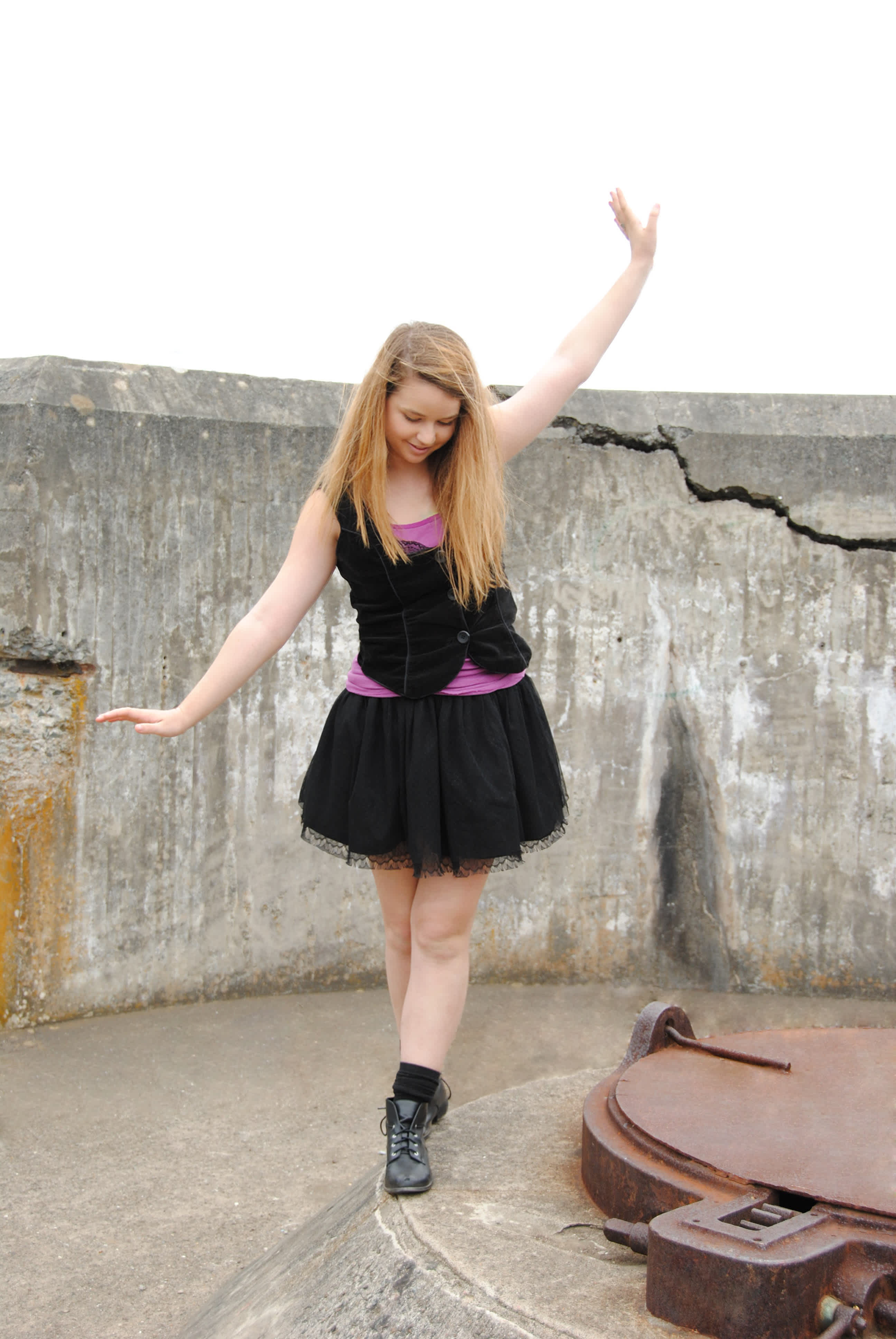 Girl in black dress posing in front of a broken-down wall. 