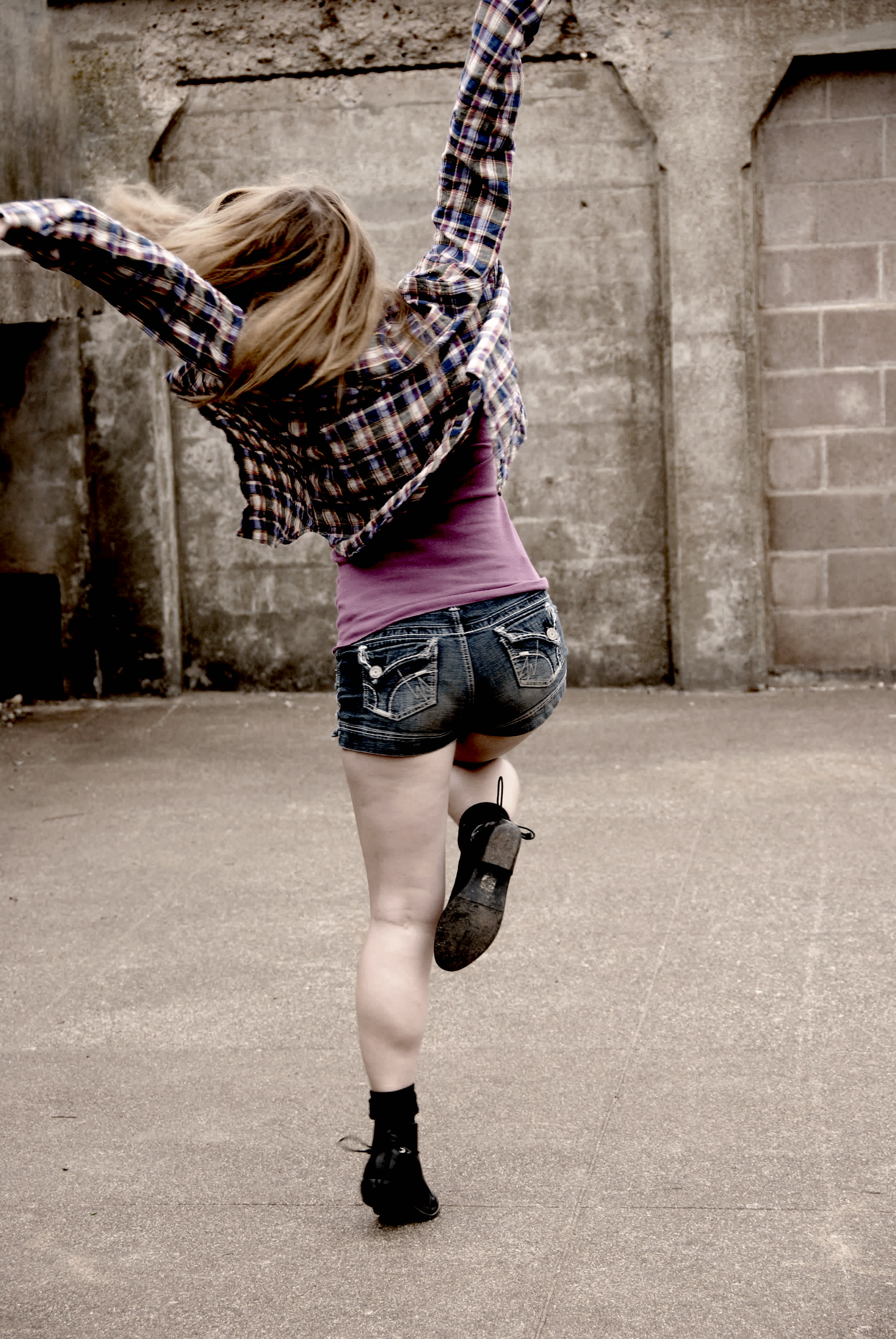 Girl jumping with arms in the arm in front of a brick wall. 