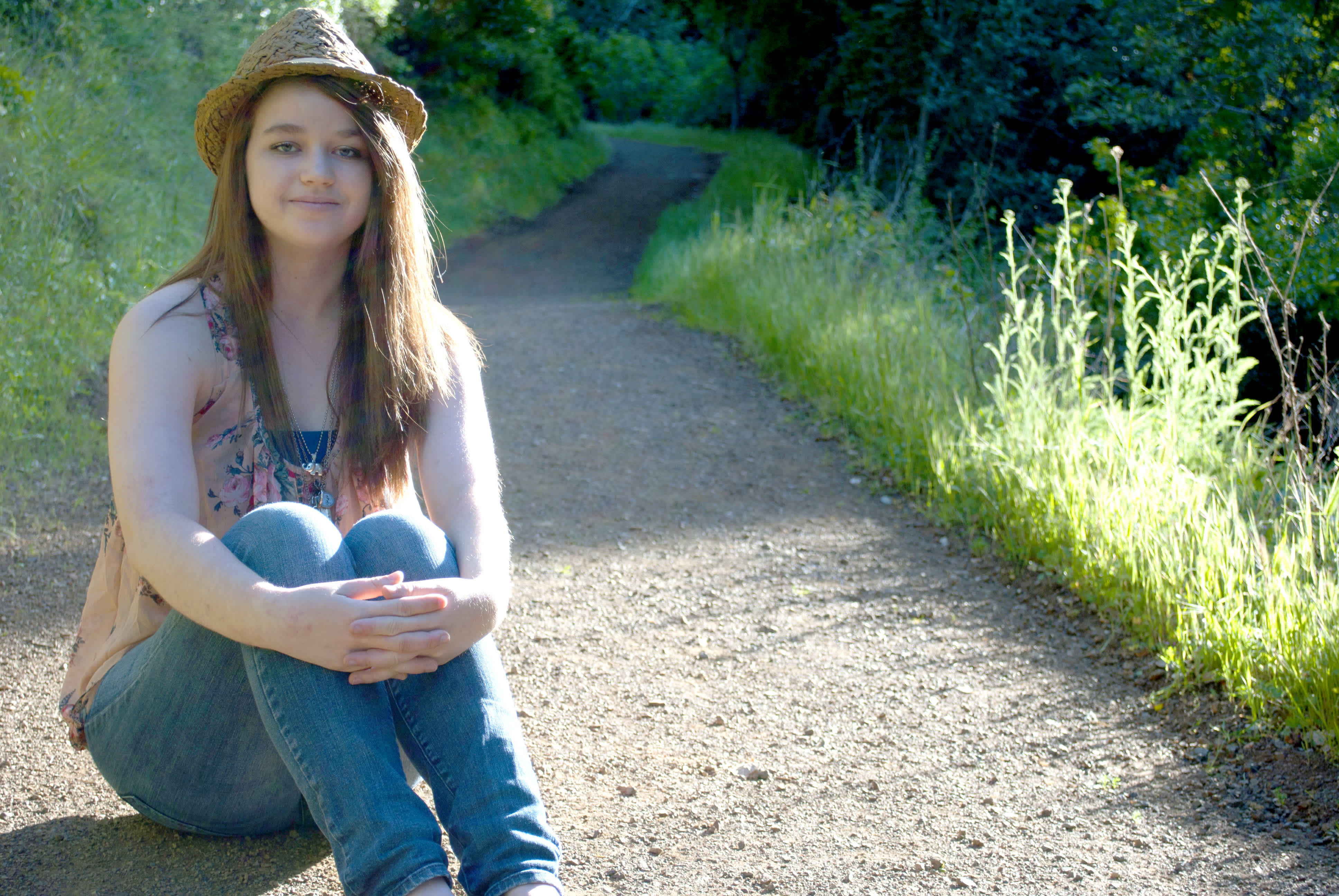 Girl sitting on a gravel path surrounded by greenery. 