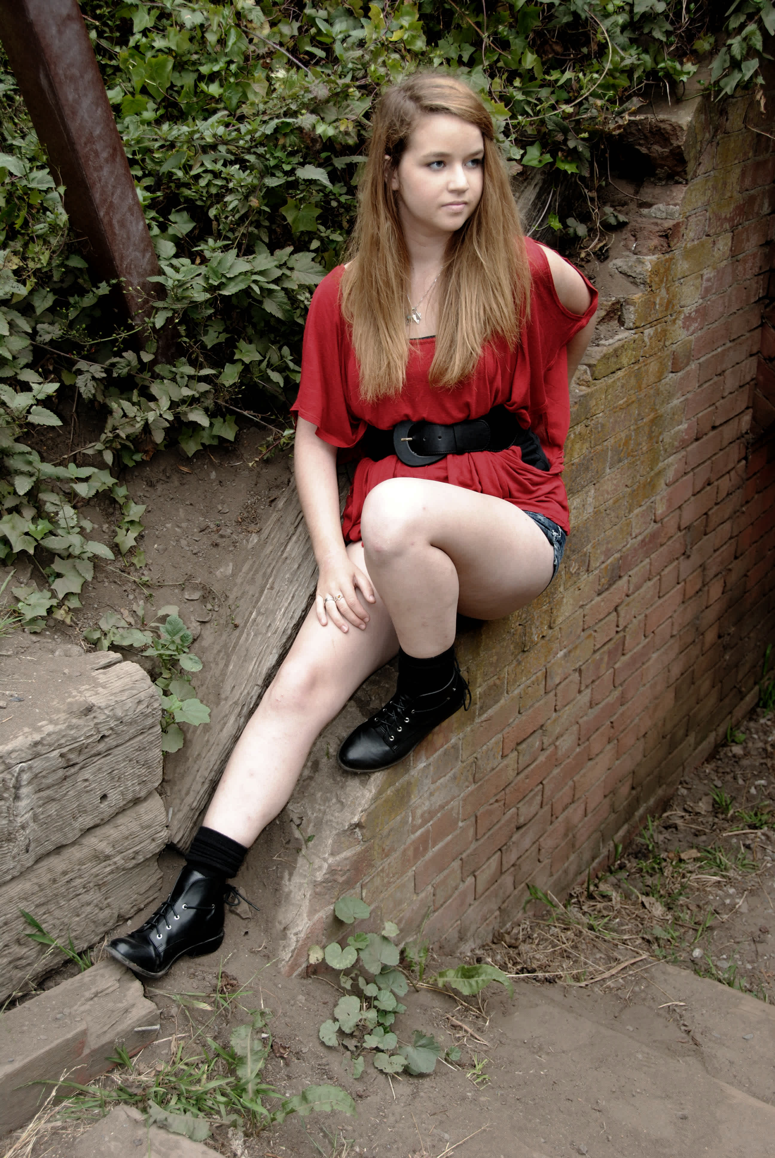 Girl in red outfit leaning against a broken brick wall. 