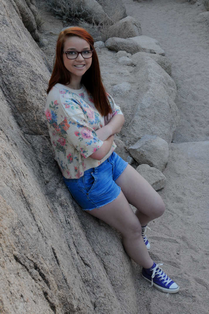 Girl in glasses leaning against a rock face. 