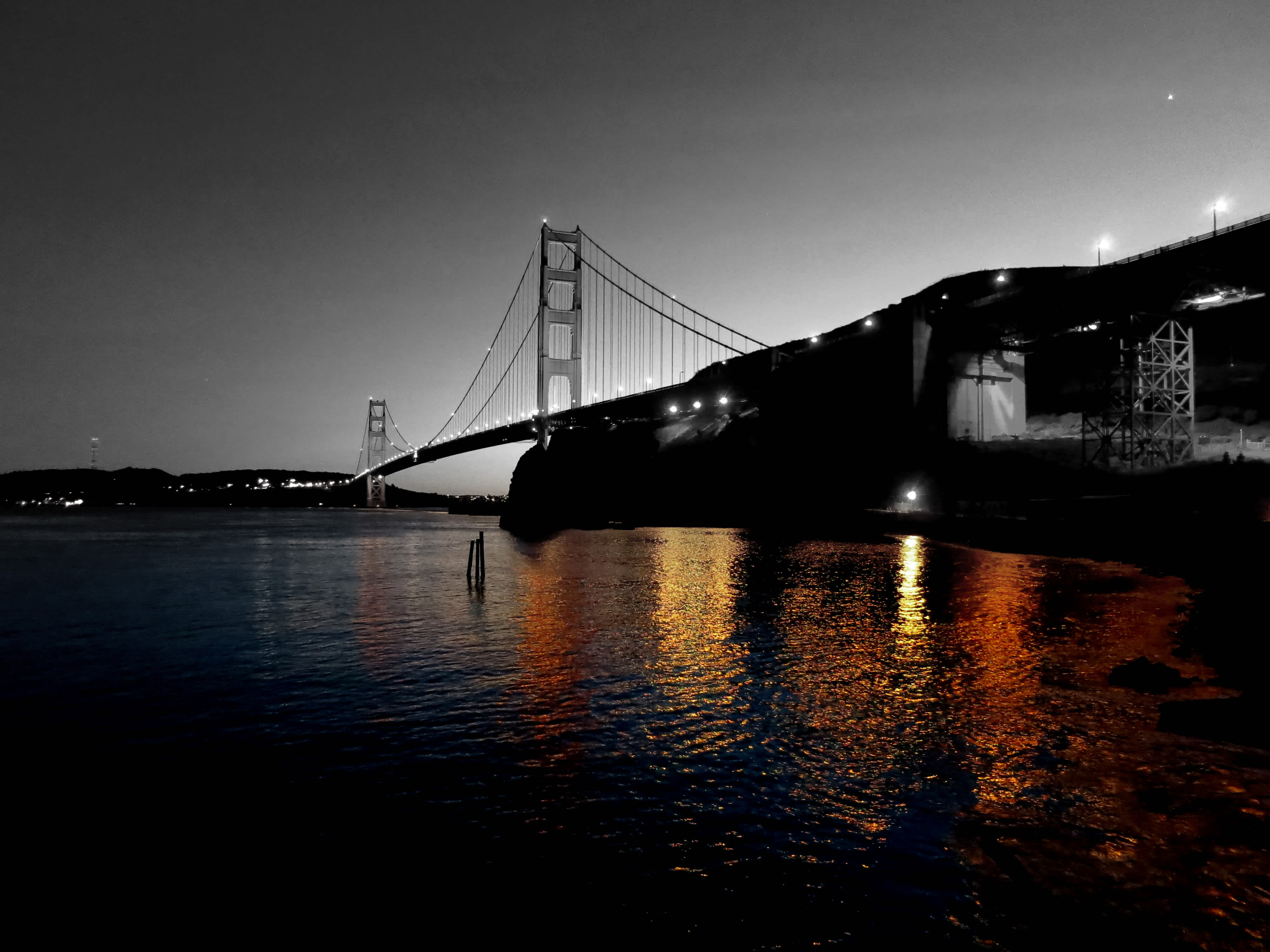 Black and white shot of Golden Gate Bridge and city with colored version reflected in the water in Golden Gate Bridge, San Francisco, California.