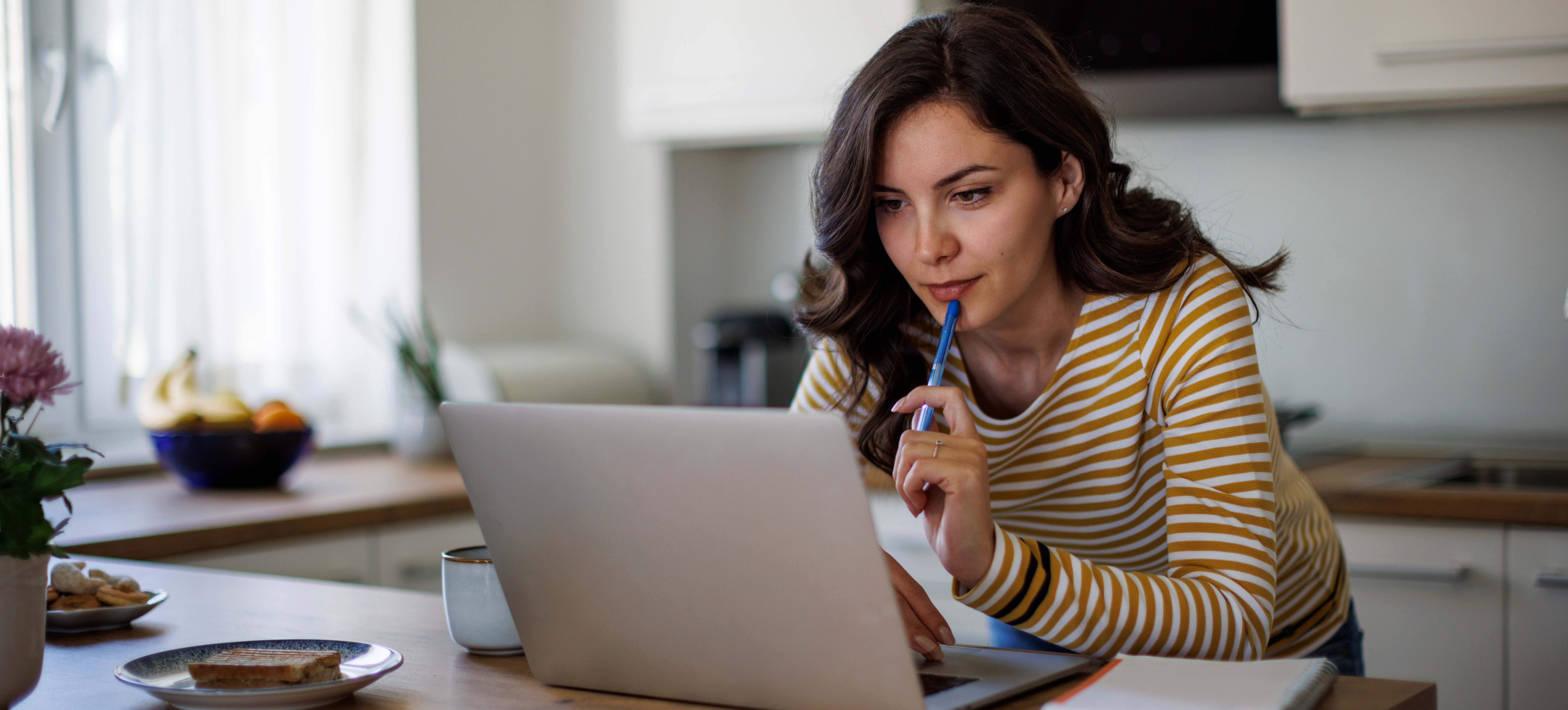 [Featured Image] A person working on a laptop in their home deciding how to end a cover letter professionally.
