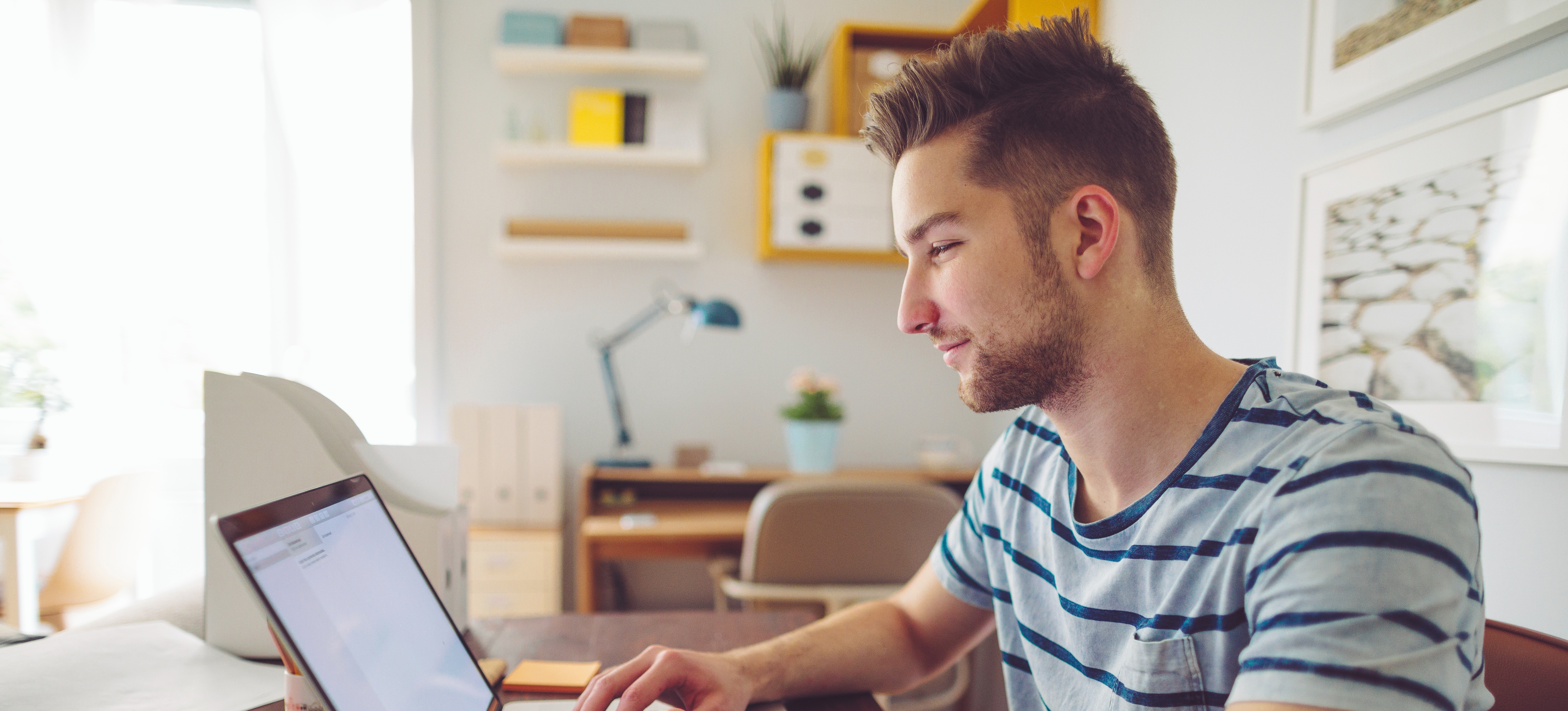 [Featured Image] A man sits at a laptop in his home office and studies so he can earn his CCIE certification.
