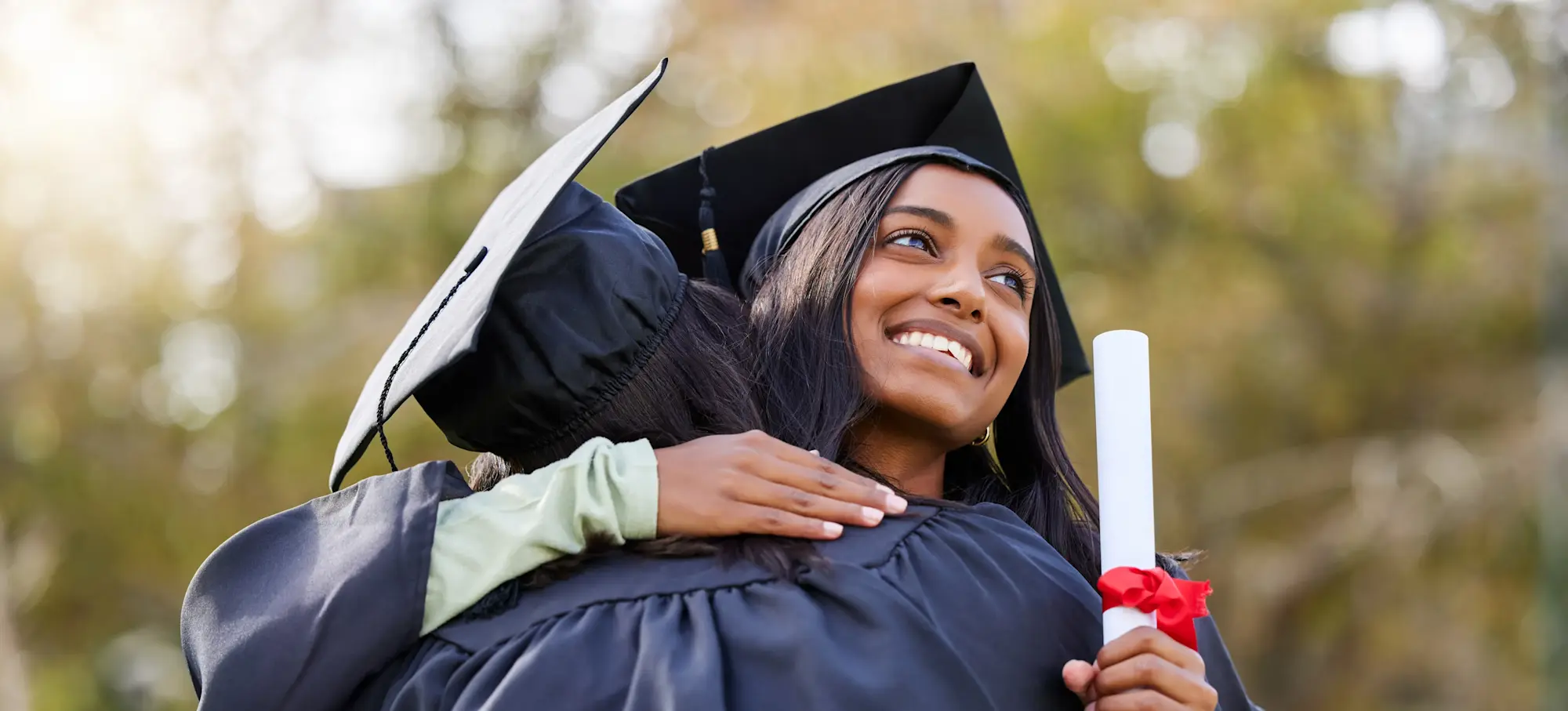 [Featured Image]: Two graduates wearing caps and gowns celebrate after receiving their MA degrees. 