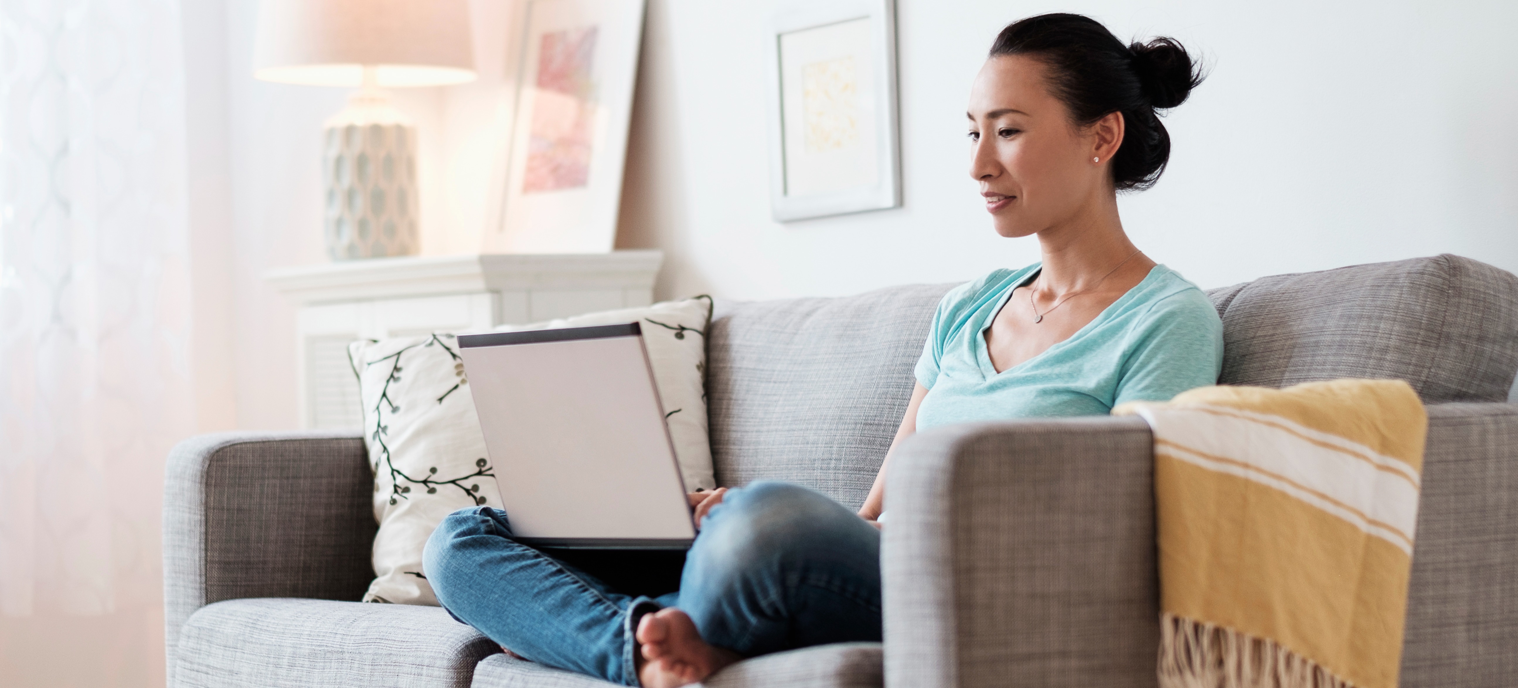[Featured Image] A woman sits on her sofa and researches the differences between Comptia A+ vs. Network+ on her laptop.
