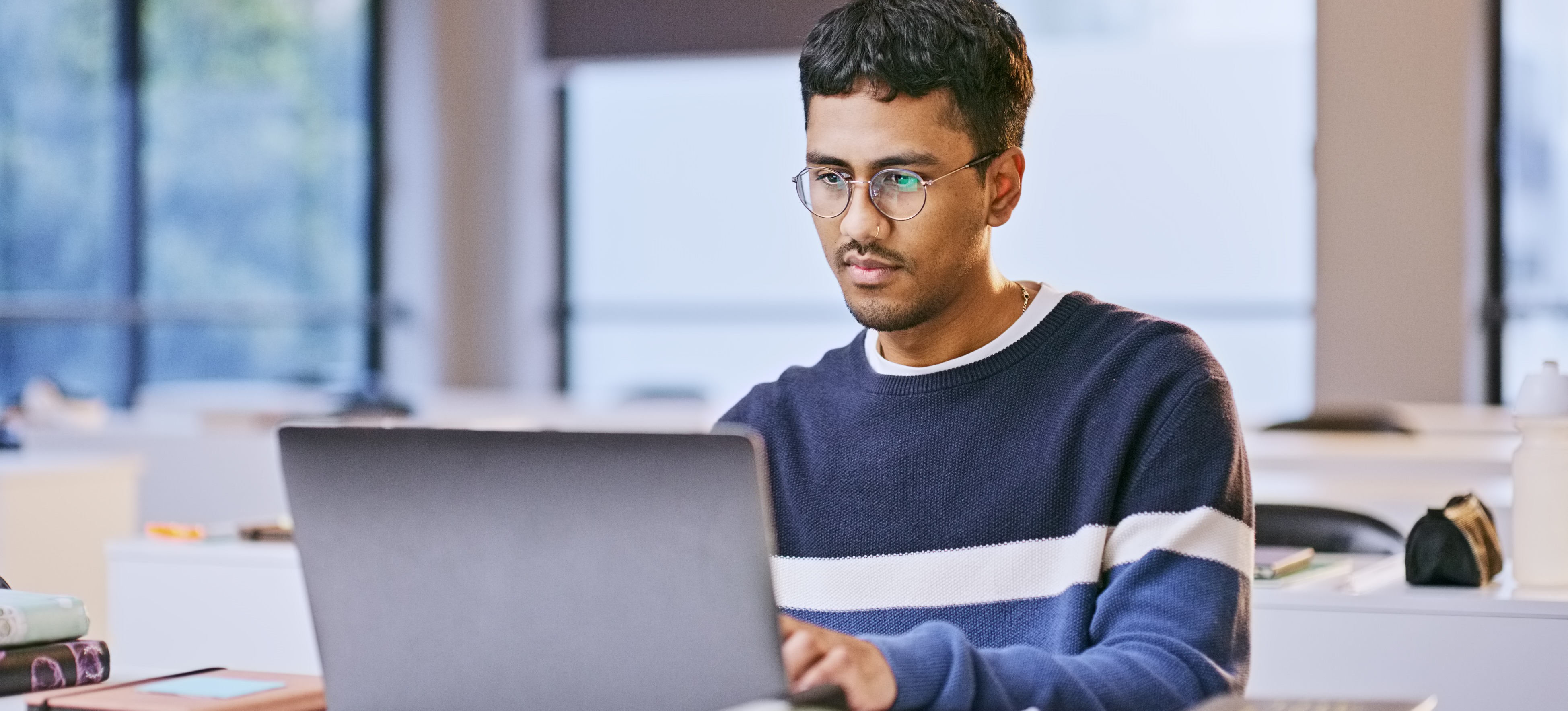 [Featured Image] A double BA student sits at a desk with a laptop, studying for their degree course programme.