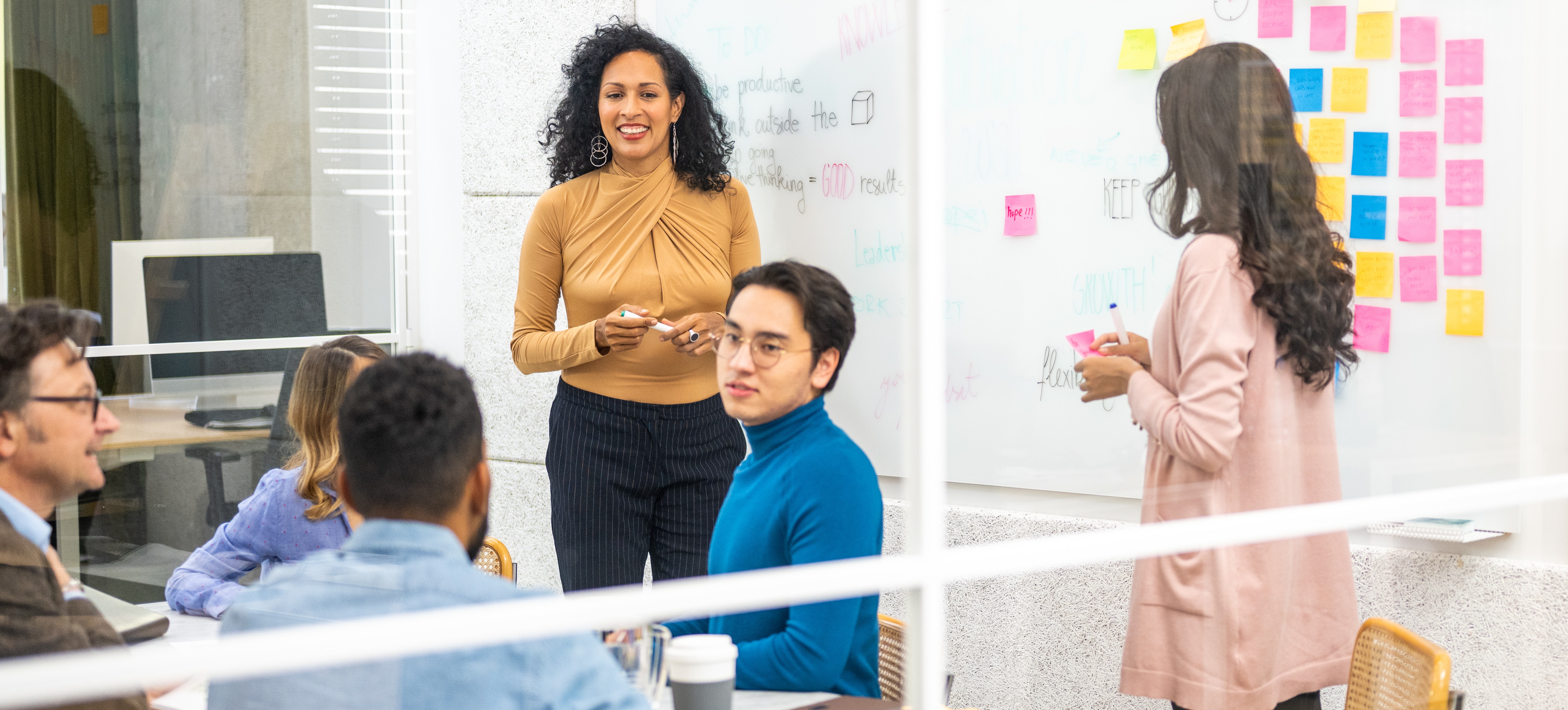 [Hauptbild] Scrum-Rollen werden dargestellt, wenn sich ein Scrum-Team in einem Konferenzraum versammelt und Aufgaben mithilfe eines Whiteboards und Haftnotizen bespricht.