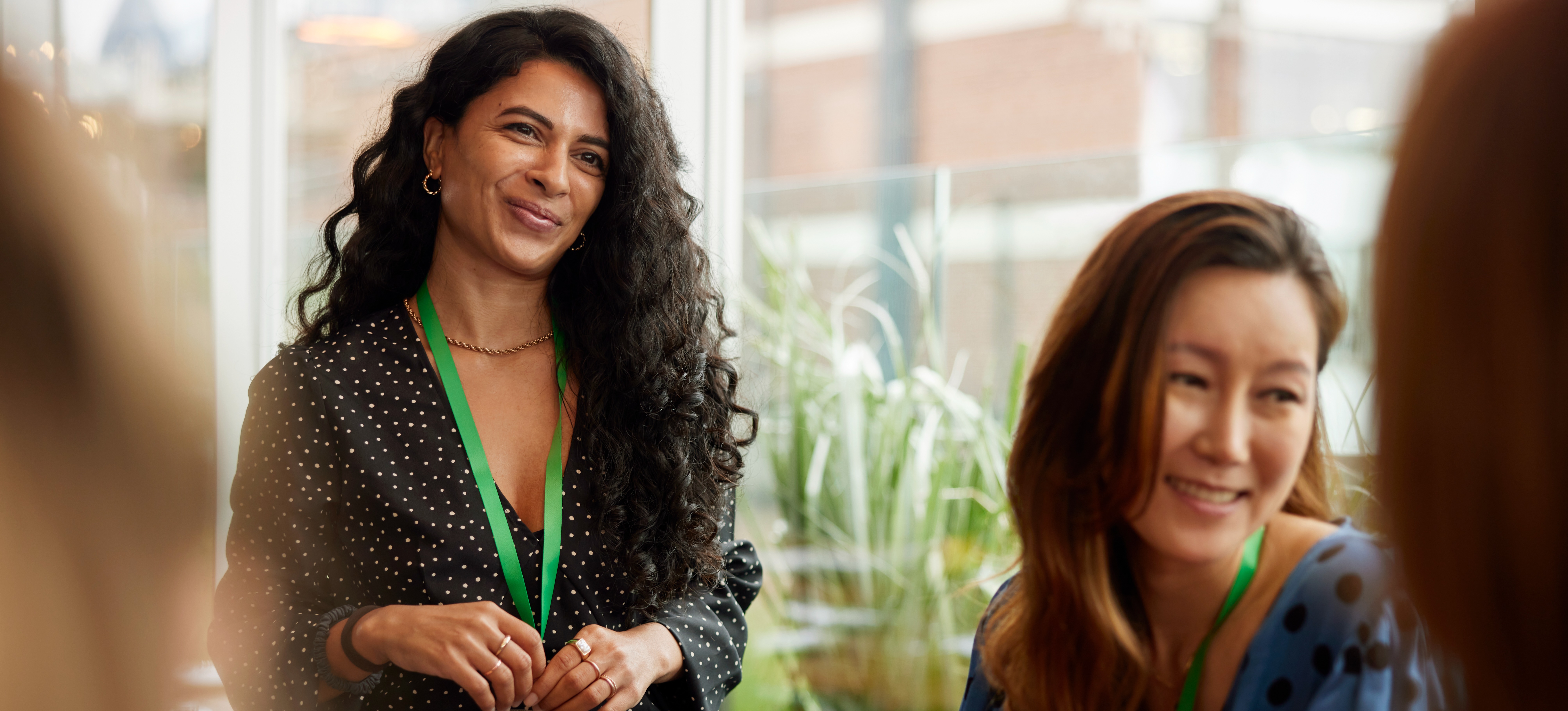 [Featured Image] A smiling woman wearing a badge in a professional environment displays her soft skills by interacting effectively with her colleagues.
