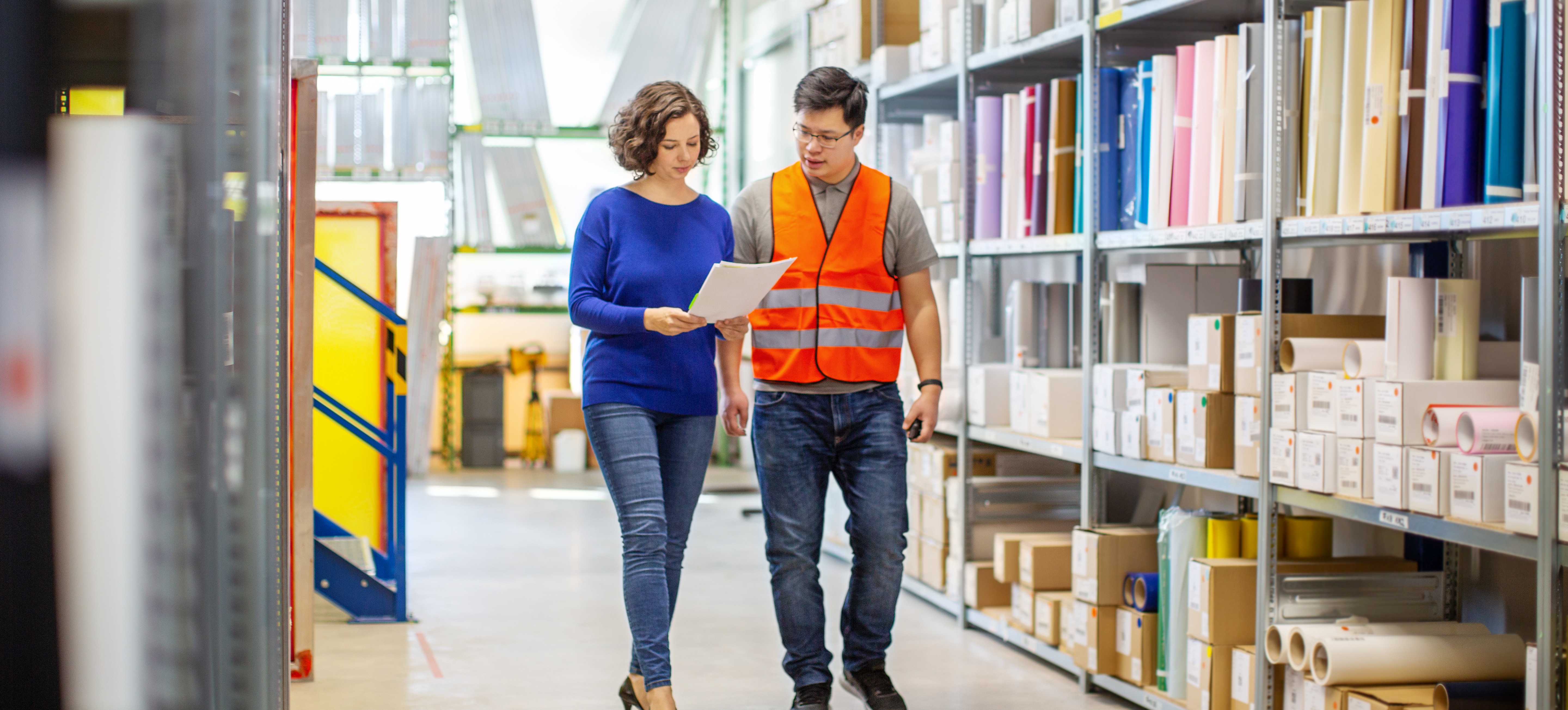 [Featured Image] A product manager is talking with a team member while walking down aisles of product.
