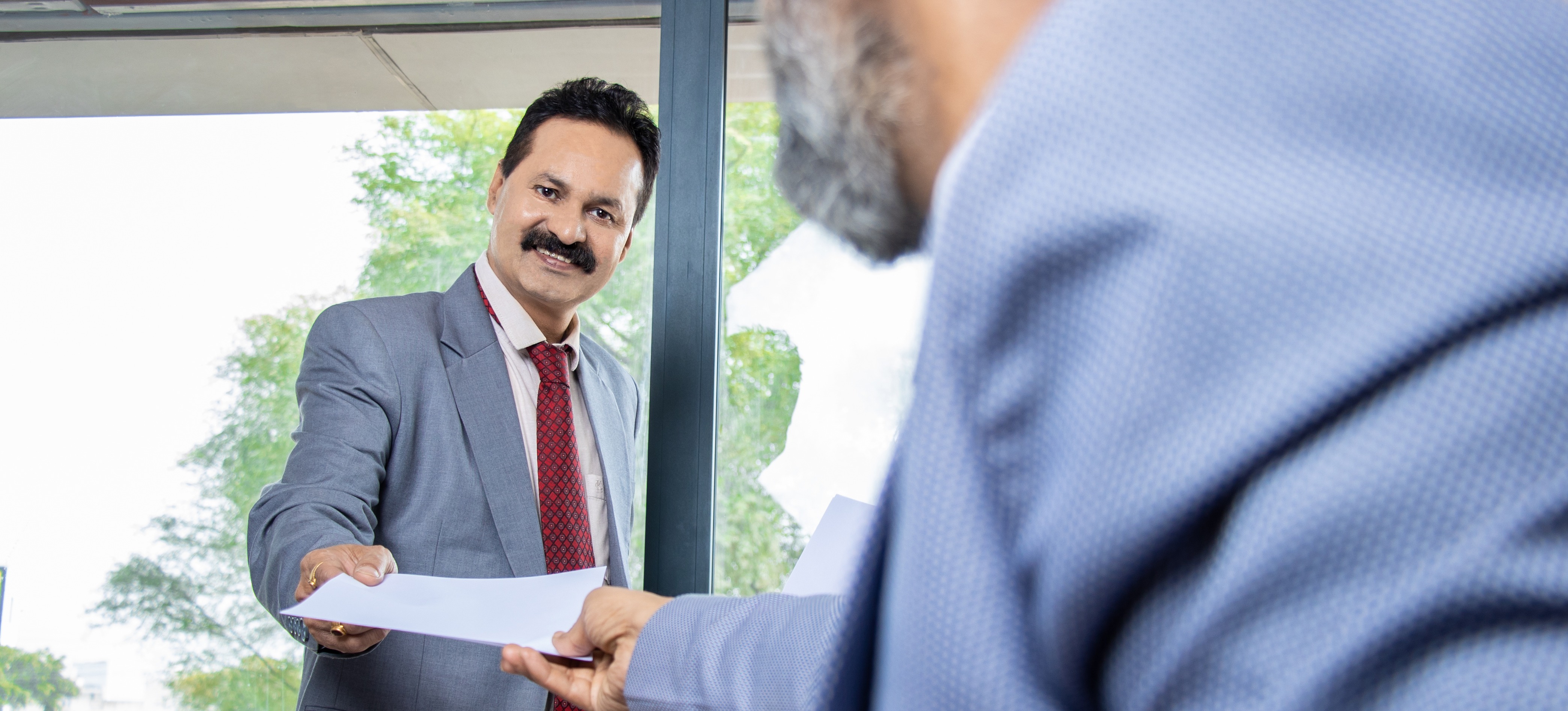 [Featured Image]: A professional gives a resume to a recruiter after learning how to feature key skills on their resume.
