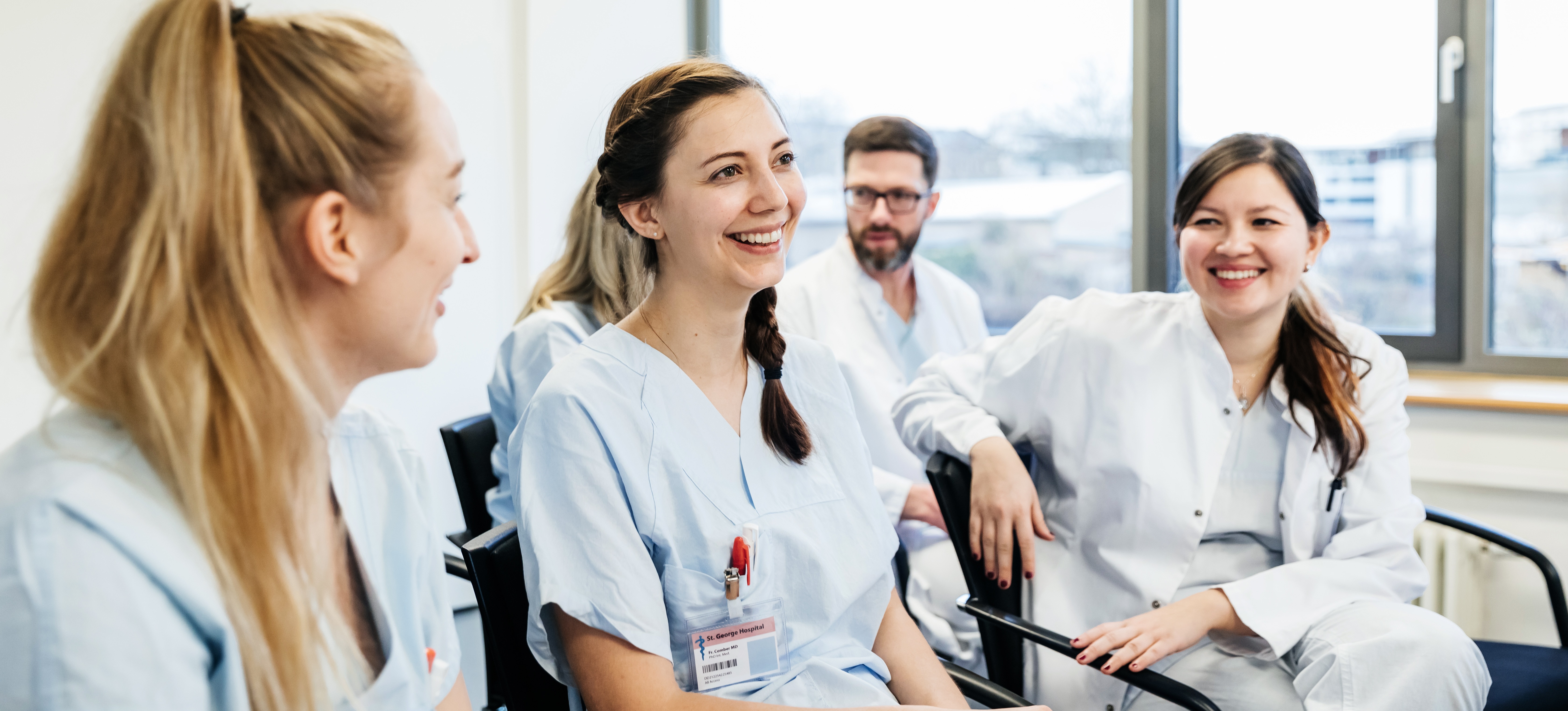 [Featured Image] A group of students who asked, “What is trade school?” and found trade school career opportunities in the medical field, laugh during a classroom session, all wearing medical scrubs.
