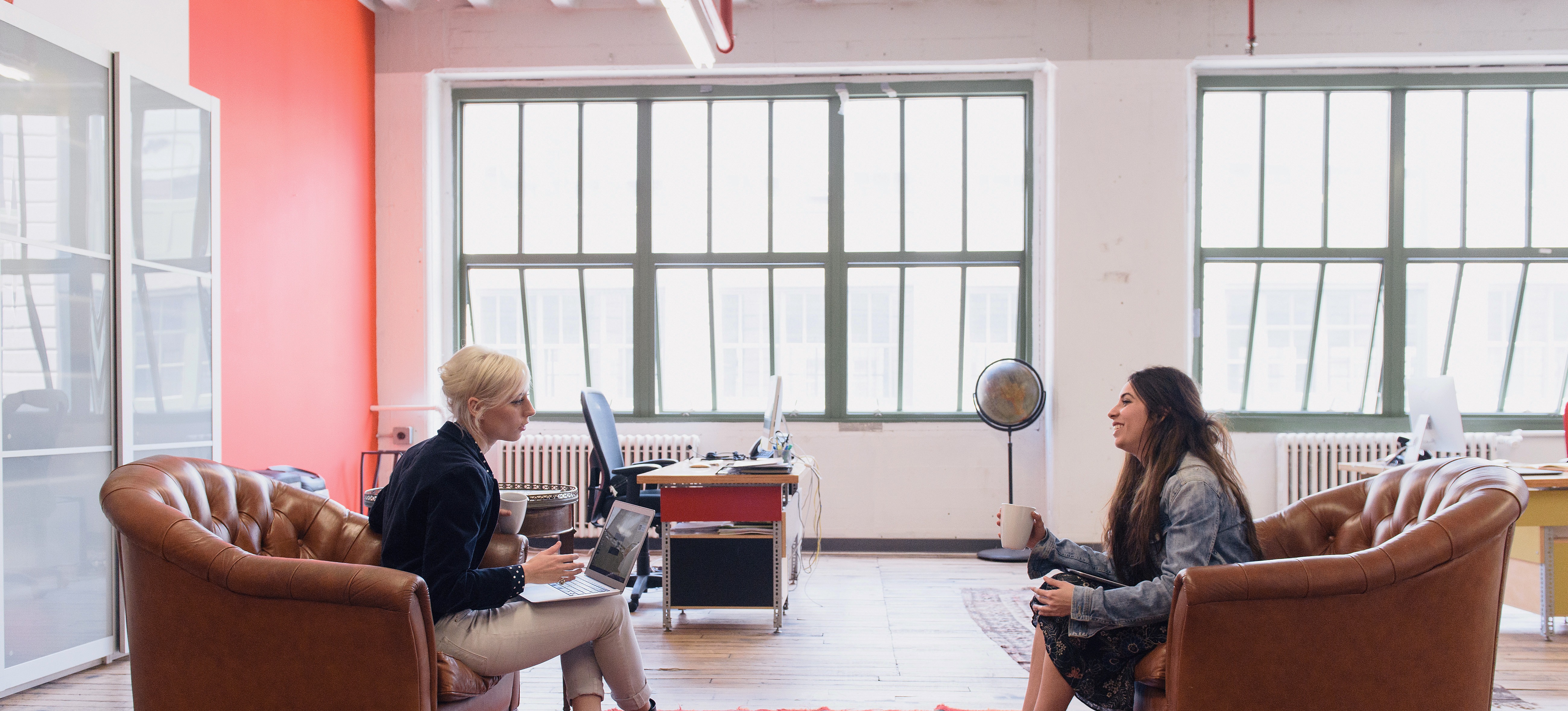 [Featured Image]:  Prospective job candidate, holding a cup of coffee, sitting across from the interviewer, asking questions during the interview. 