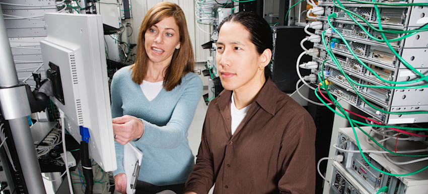 [Featured Image] A business manager is in the server room conducting a hands-on interview with a technician for a network administrator position.
