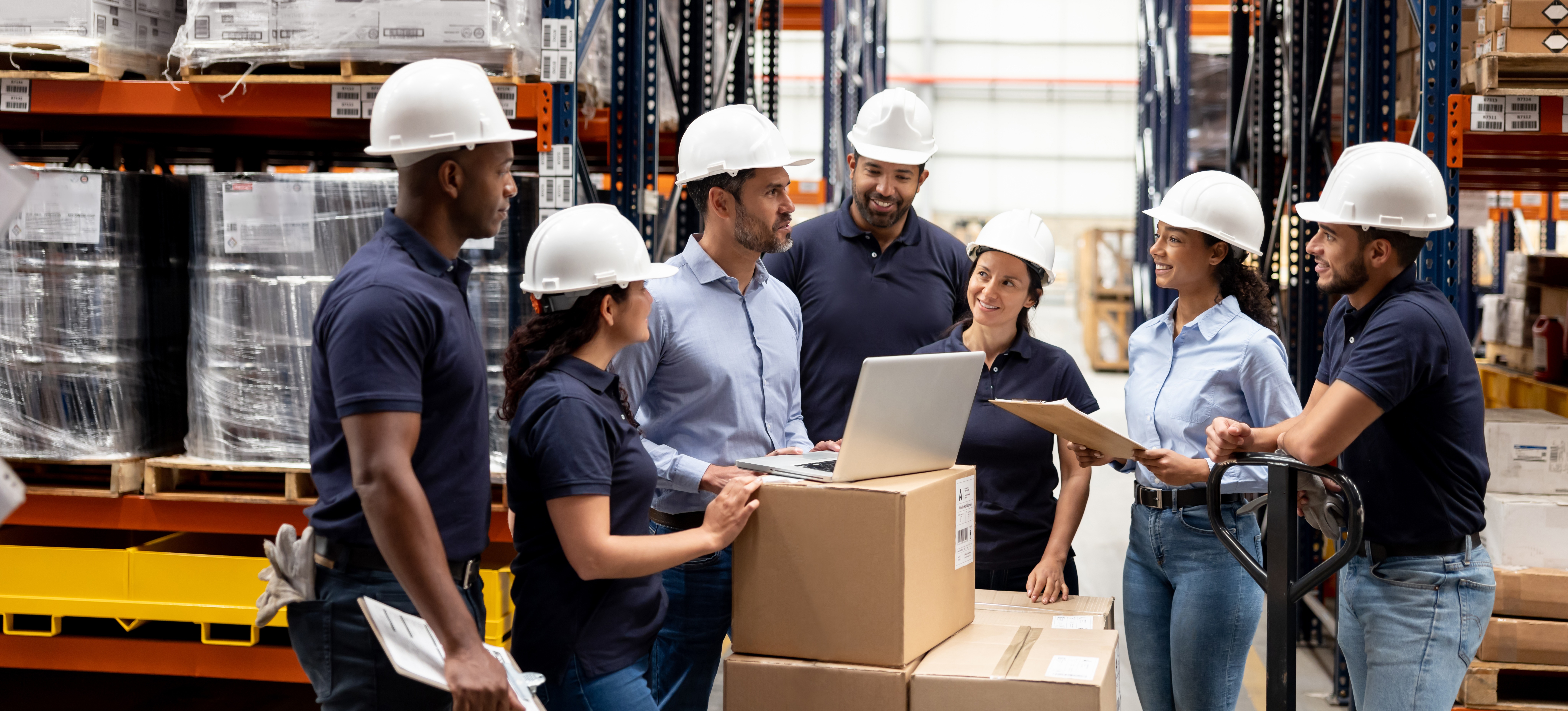 [Featured Text]: A group of people in a warehouse has a team meeting to discuss their roles within the supply chain control tower.