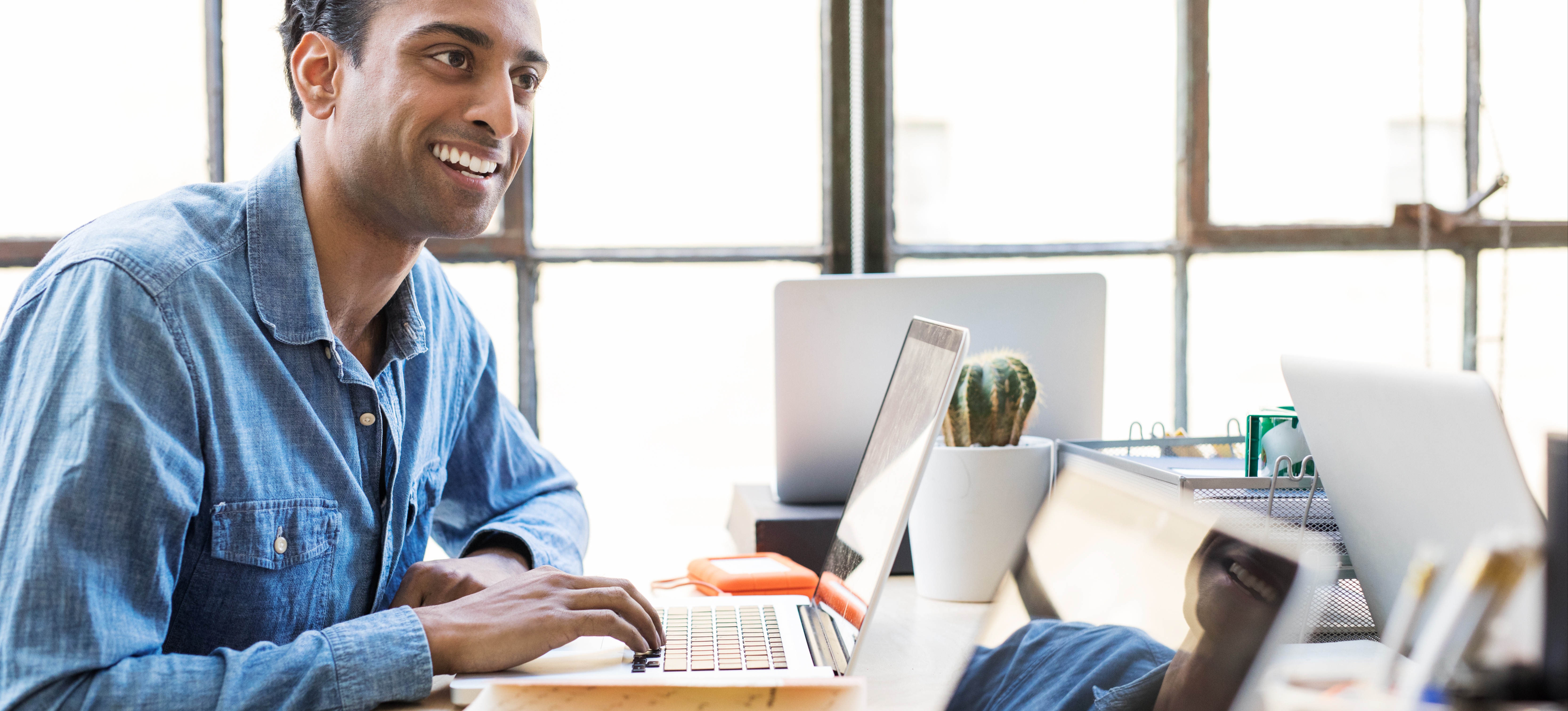 [Featured Image] A smiling data scientist works at his computer on digital transformation tasks.