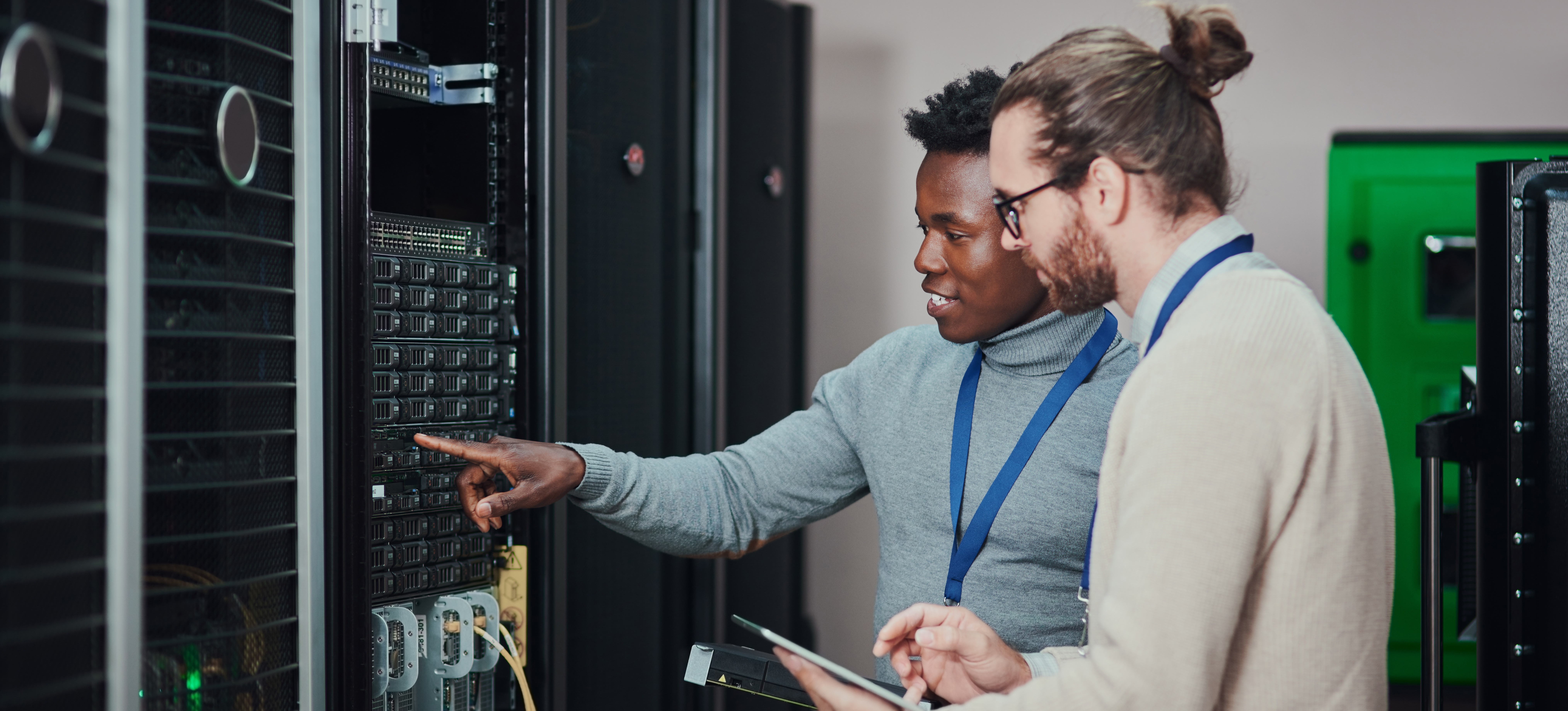 [Featured Image] Technicians in a technological workspace, reviewing data on a tablet, demonstrating the responsibilities and skills of a data center technician.