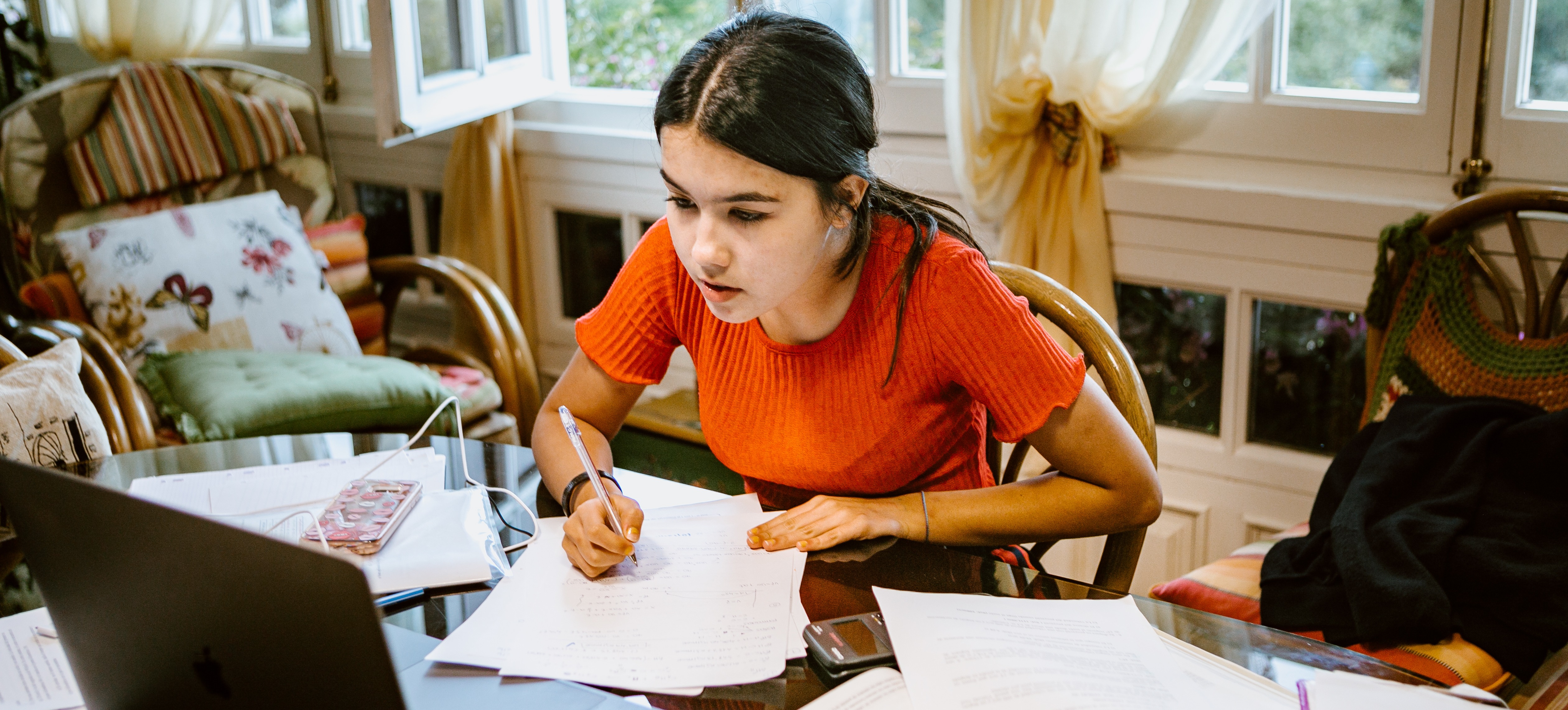 [Featured Image] A college student is studying with their laptop, books,  and pencil at their dining room table.
