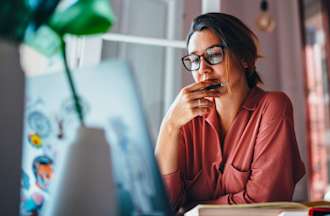 [Featured image] IT learner in a pink blouse sits at a desk with a laptop and book and considers which entry-level IT certification to get.