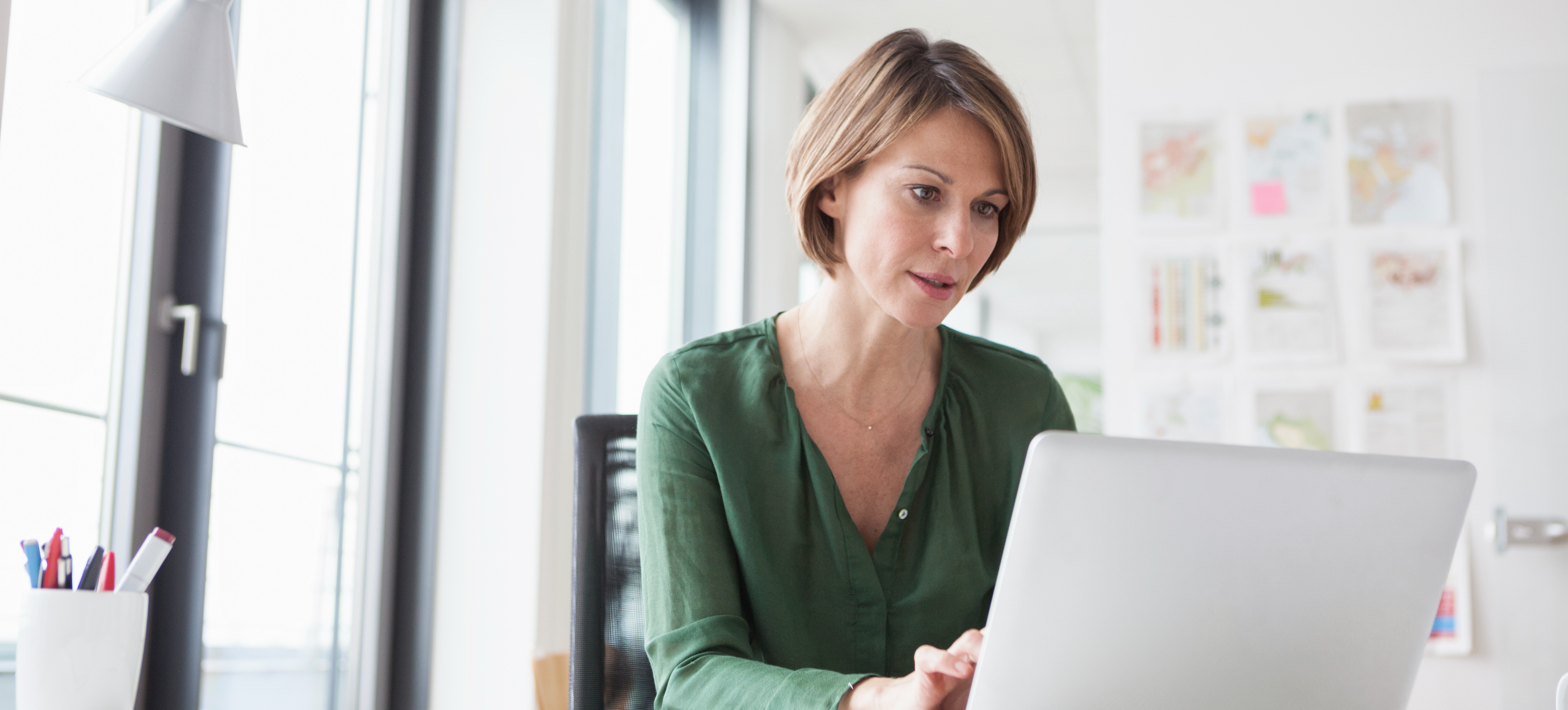 [Featured Image] A marketer sits at their laptop at their desk and goes over the results of AB testing conducted by their team. 
