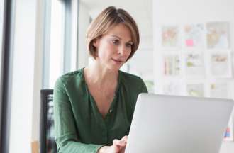 [Featured Image] A marketer sits at her laptop at her desk and goes over the results of AB testing conducted by her team. 
