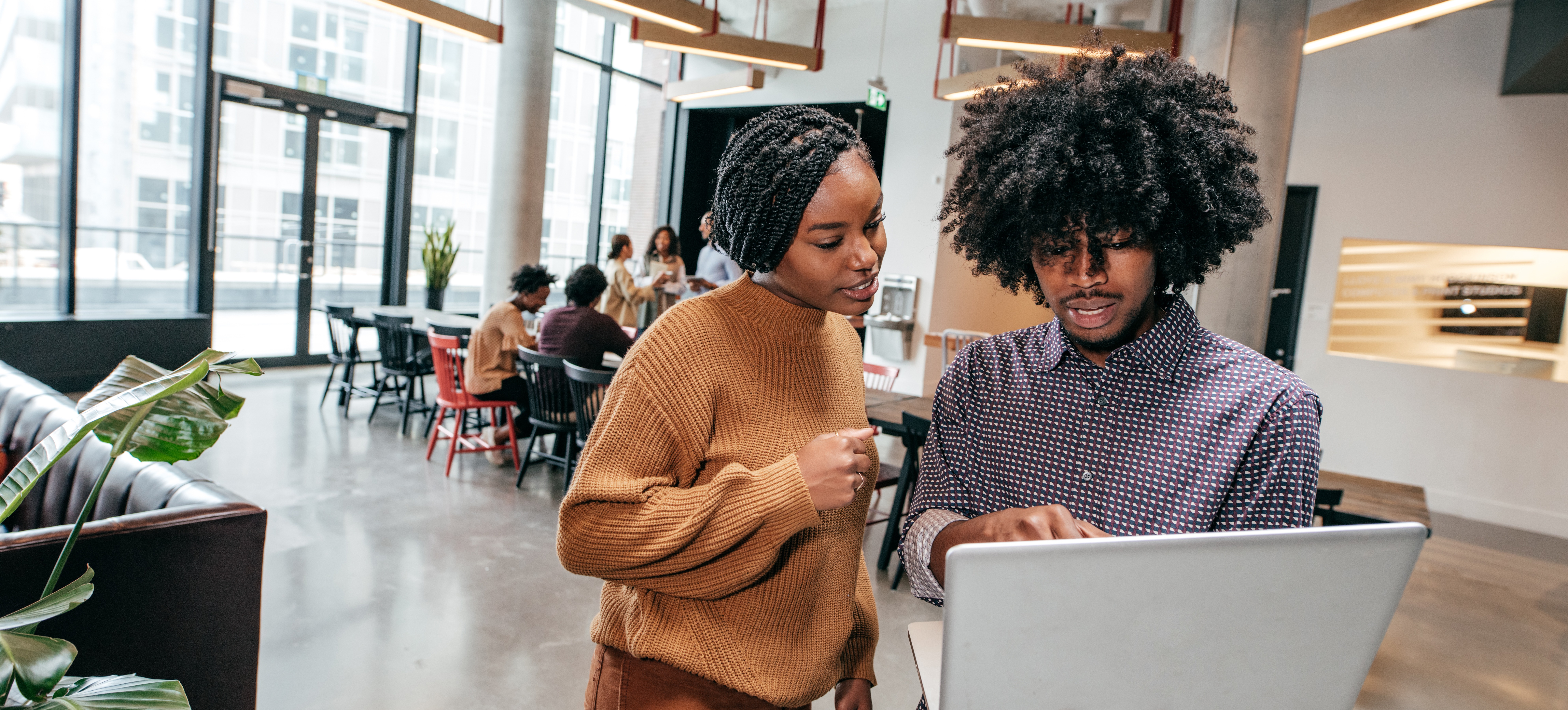 [Hauptbild] Mitarbeiter besprechen einen Plan auf einem Laptop, während ein Team hinter ihnen arbeitet.