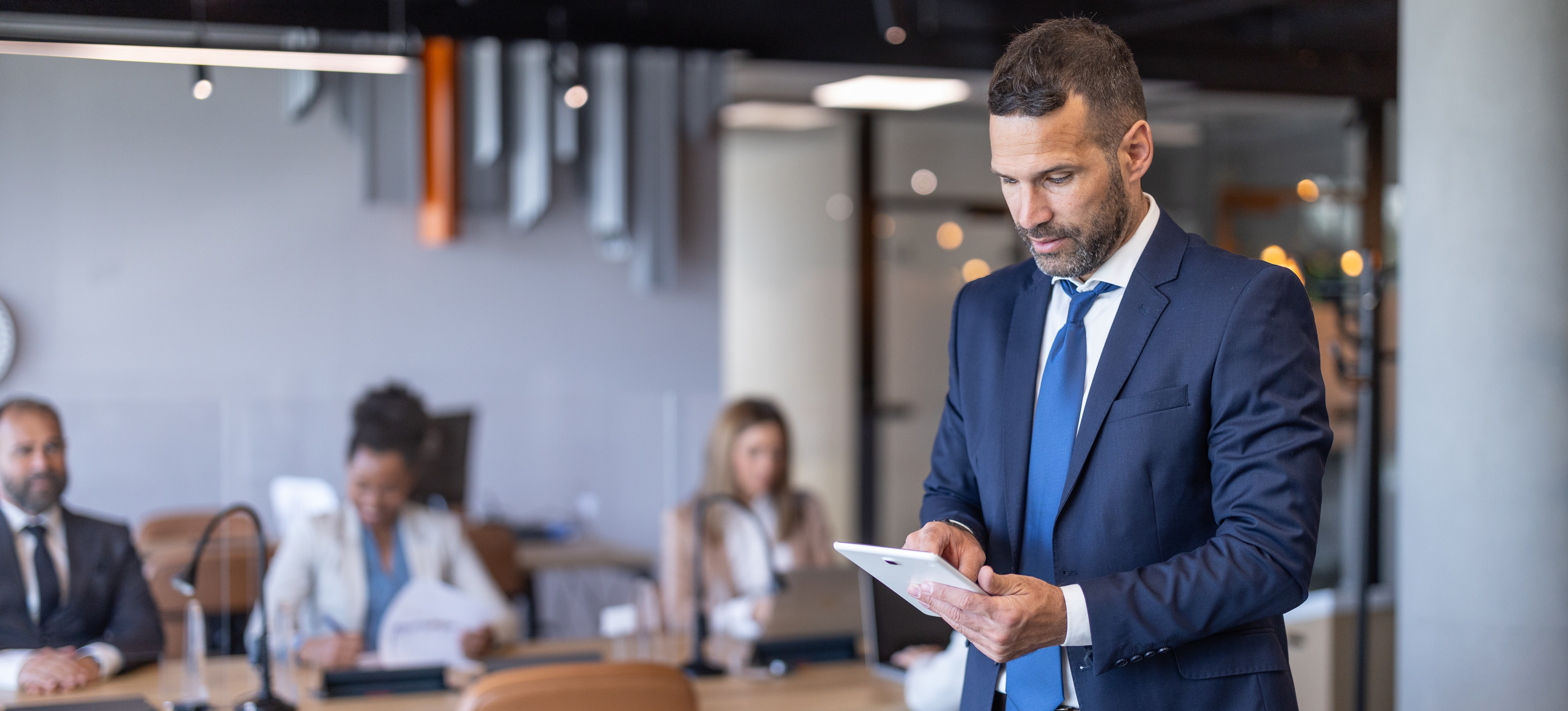 [Image en vedette] Un professionnel en costume-cravate se tient debout dans un bureau, un appareil électronique à la main, occupé à analyser un poste.
