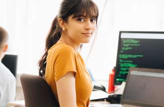 [Featured Image] A dark-haired programmer turns away from their laptop and computer monitor while learning how to code. 