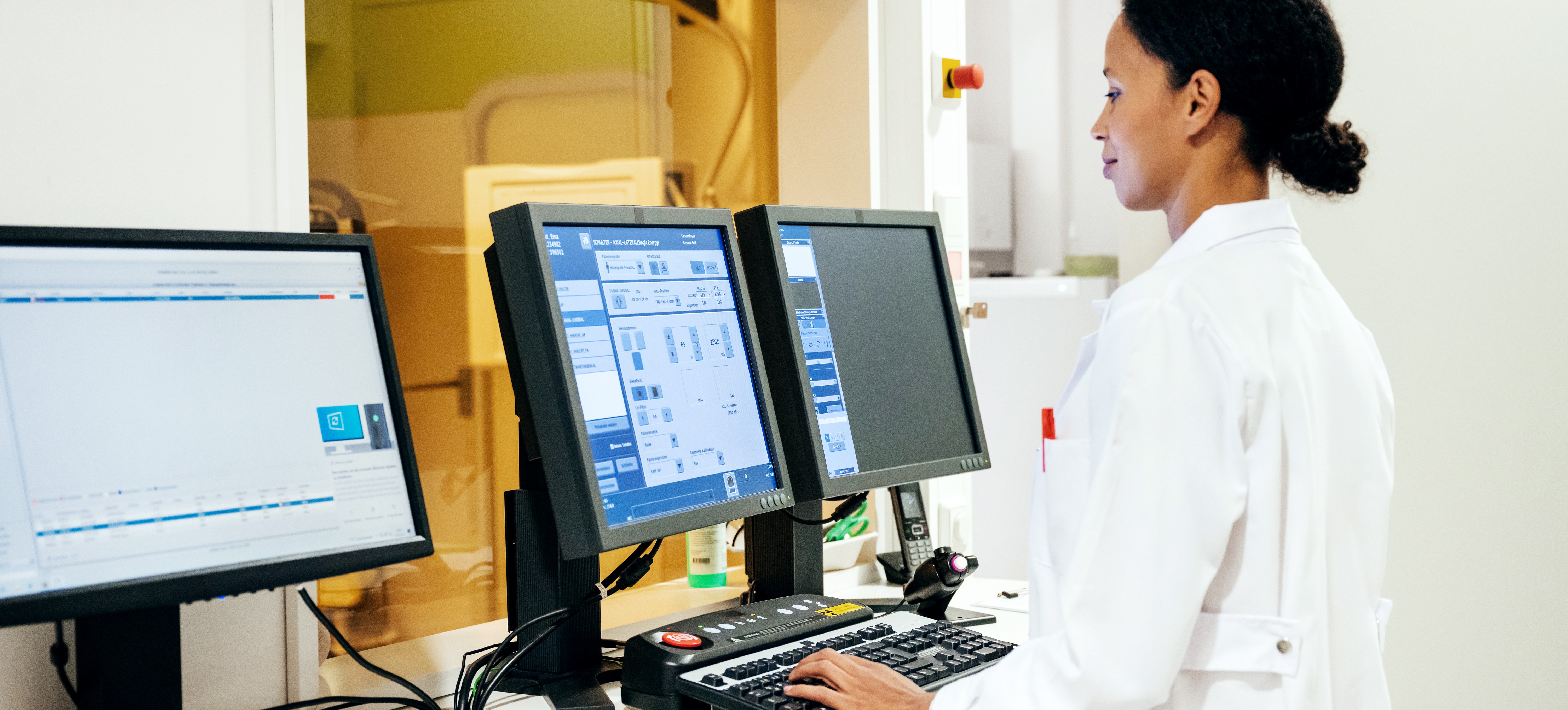 [Featured Image] A doctor in a white lab coat stands in front of several computer monitors viewing information created by data lake architecture in a hospital radiology department.

