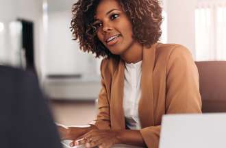 [Featured image] A human capital management (HCM) staffer sits at a desk and speaks with another company employee.