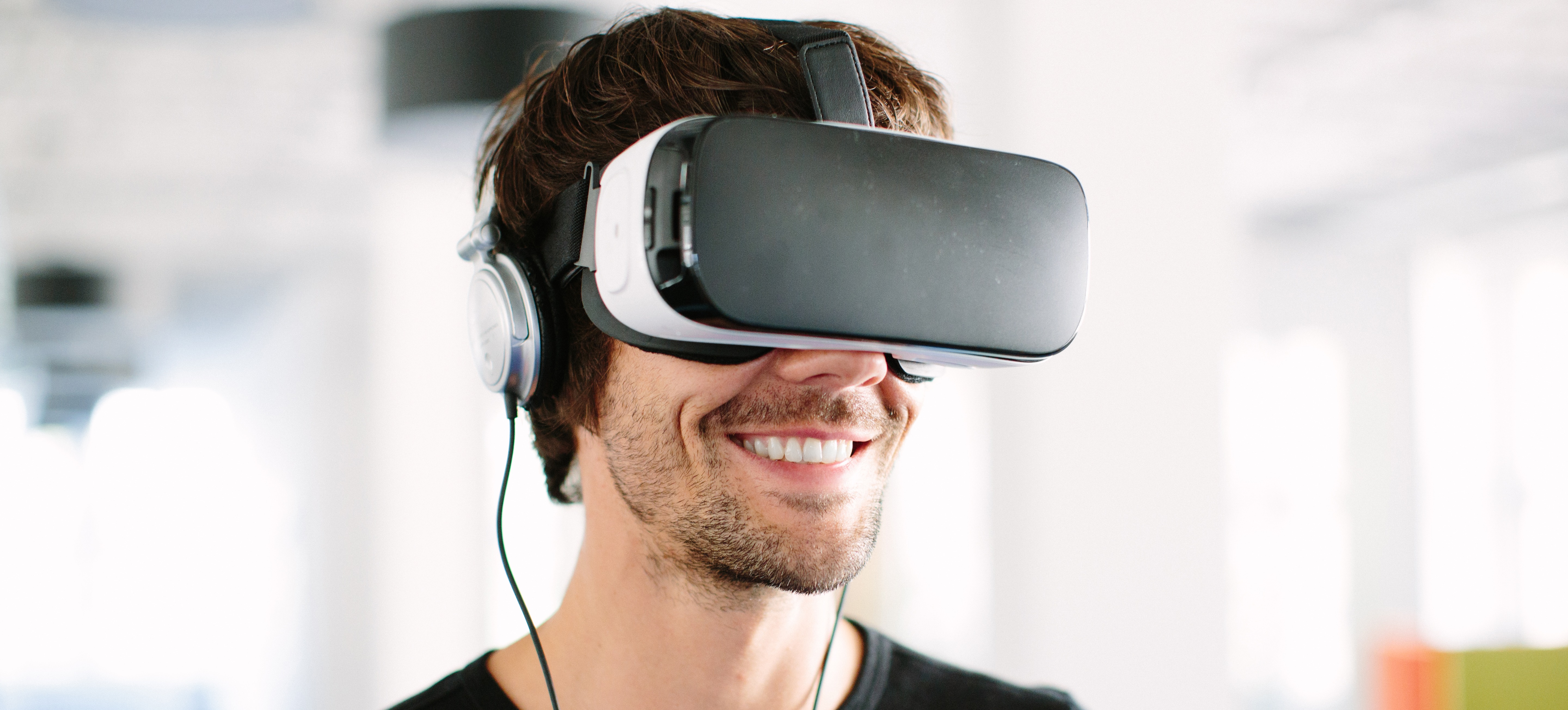 [Featured Image] A smiling man in a black shirt wears a VR headset and headphones, and wonders how to become a game developer.
