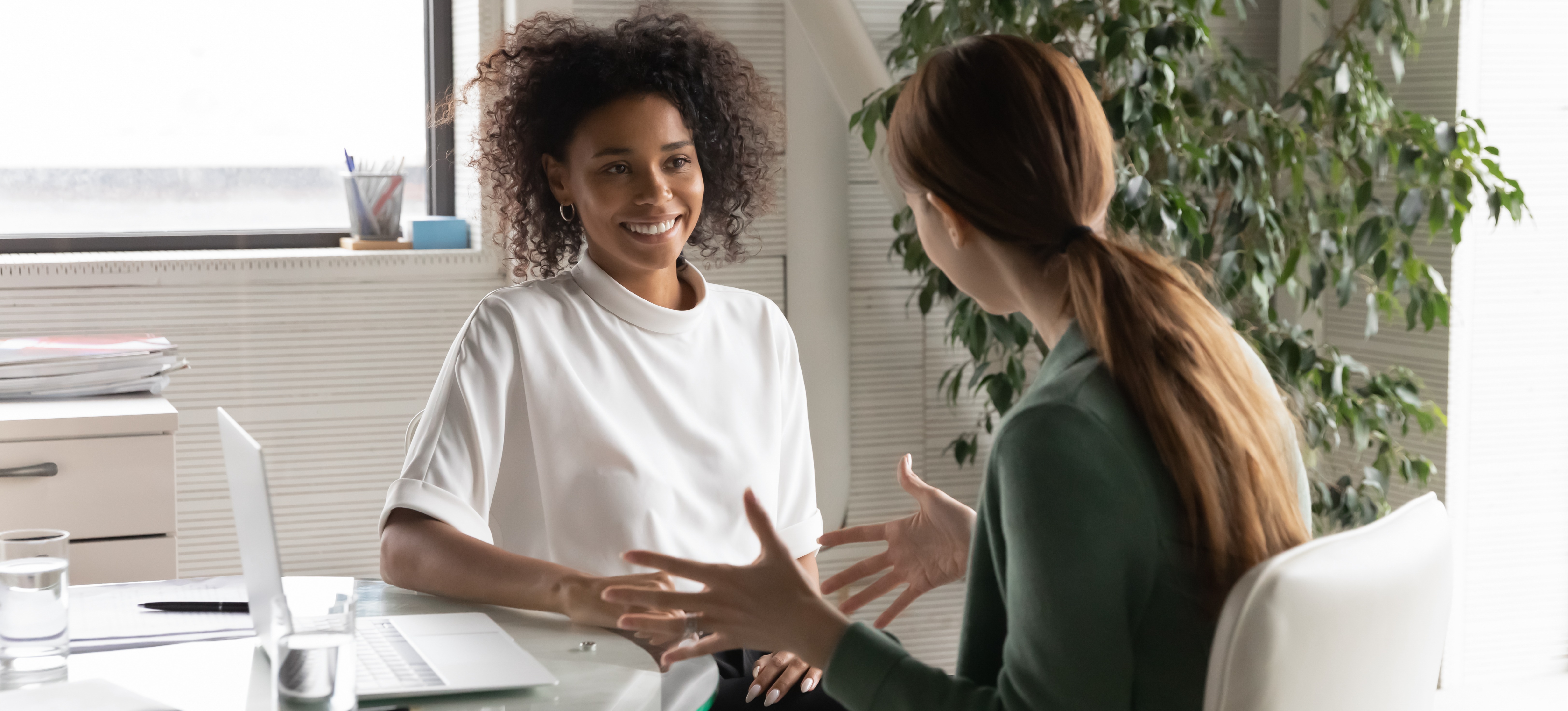 [Featured Image] Two female colleagues sit down at a laptop in an office while one asks, "What is ChatGPT?".