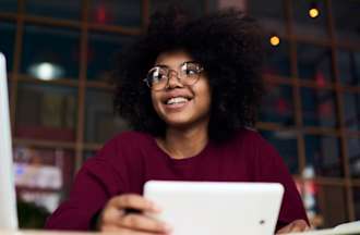 [Featured Image] A person in a red sweater and glasses sits at a desk and works with data on both their phone and their laptop using cloud computing services.