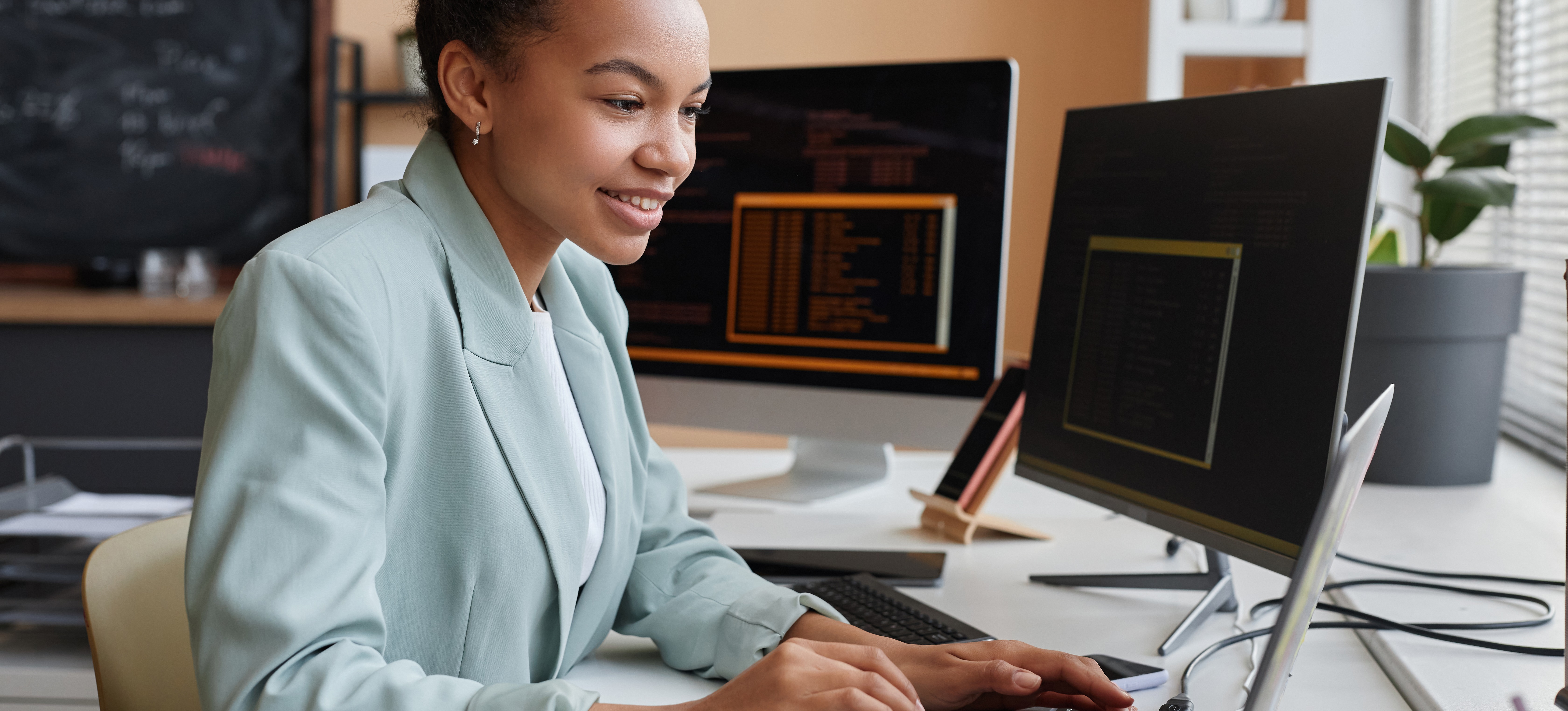 [Featured Image] An IT professional works at her computer deciding if she should take the CCNA or Network+ certifications to help advance her career.
