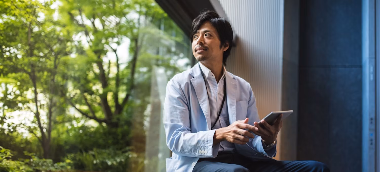 [Hauptbild] Ein Mann sitzt am Fenster und arbeitet an einem Tablet.